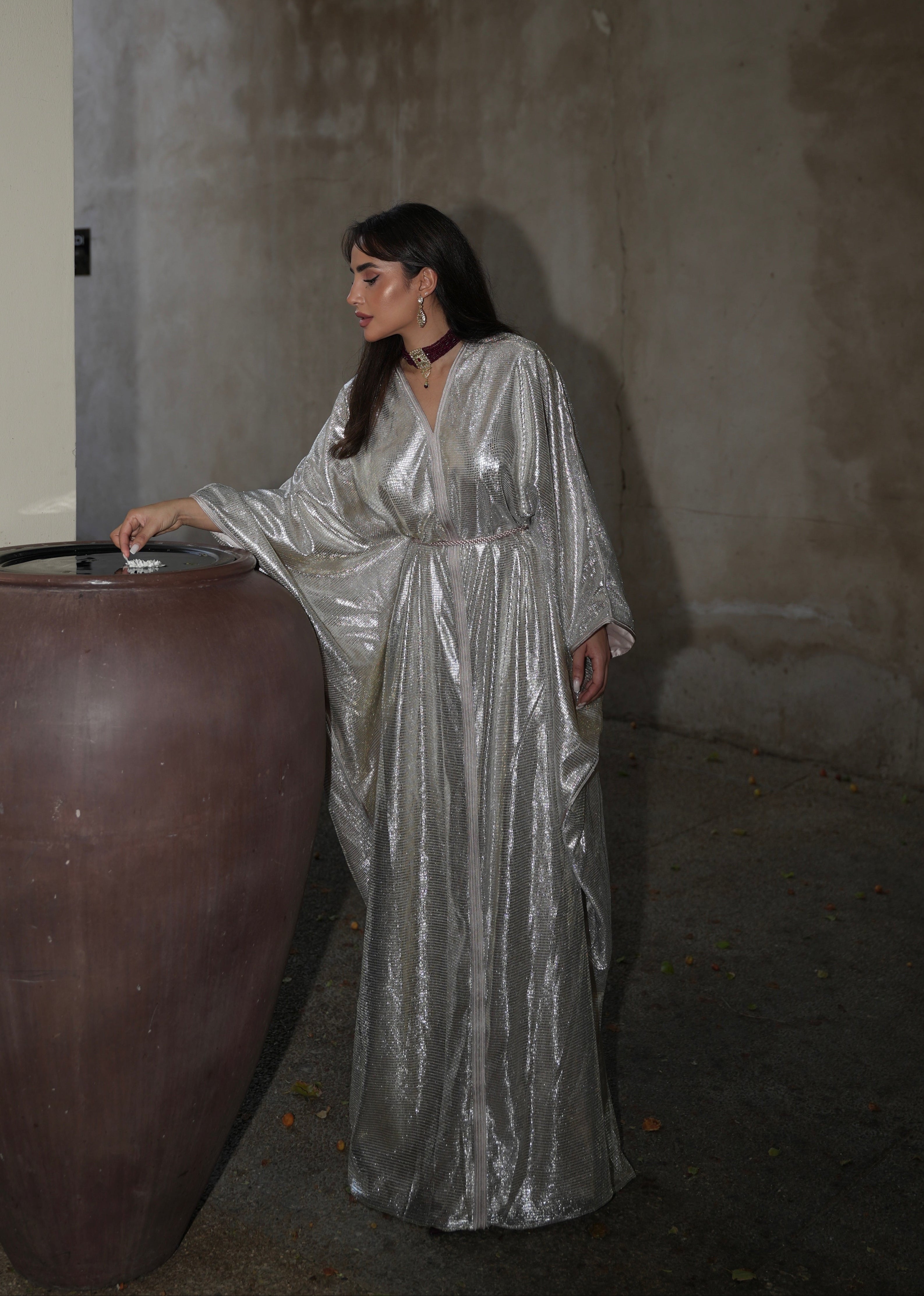 قفطان من التول الفضي المطرز بالخرز مع تفاصيل الفراشات التي تم التقاطها أثناء الحركة، مما يبرز انسيابية القماش والانعكاسات الرقيقة للخرز الفضي والفراشات.