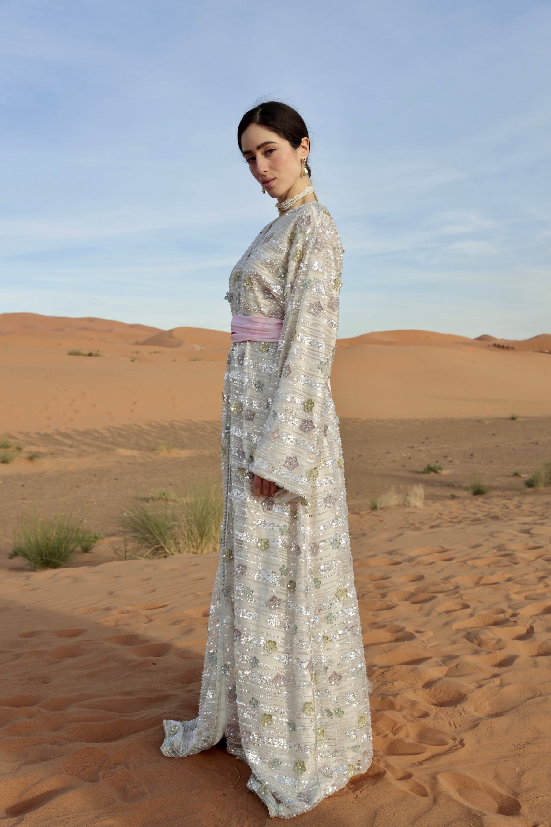 Caftan en tulle perlé argenté à motifs floraux porté de profil.