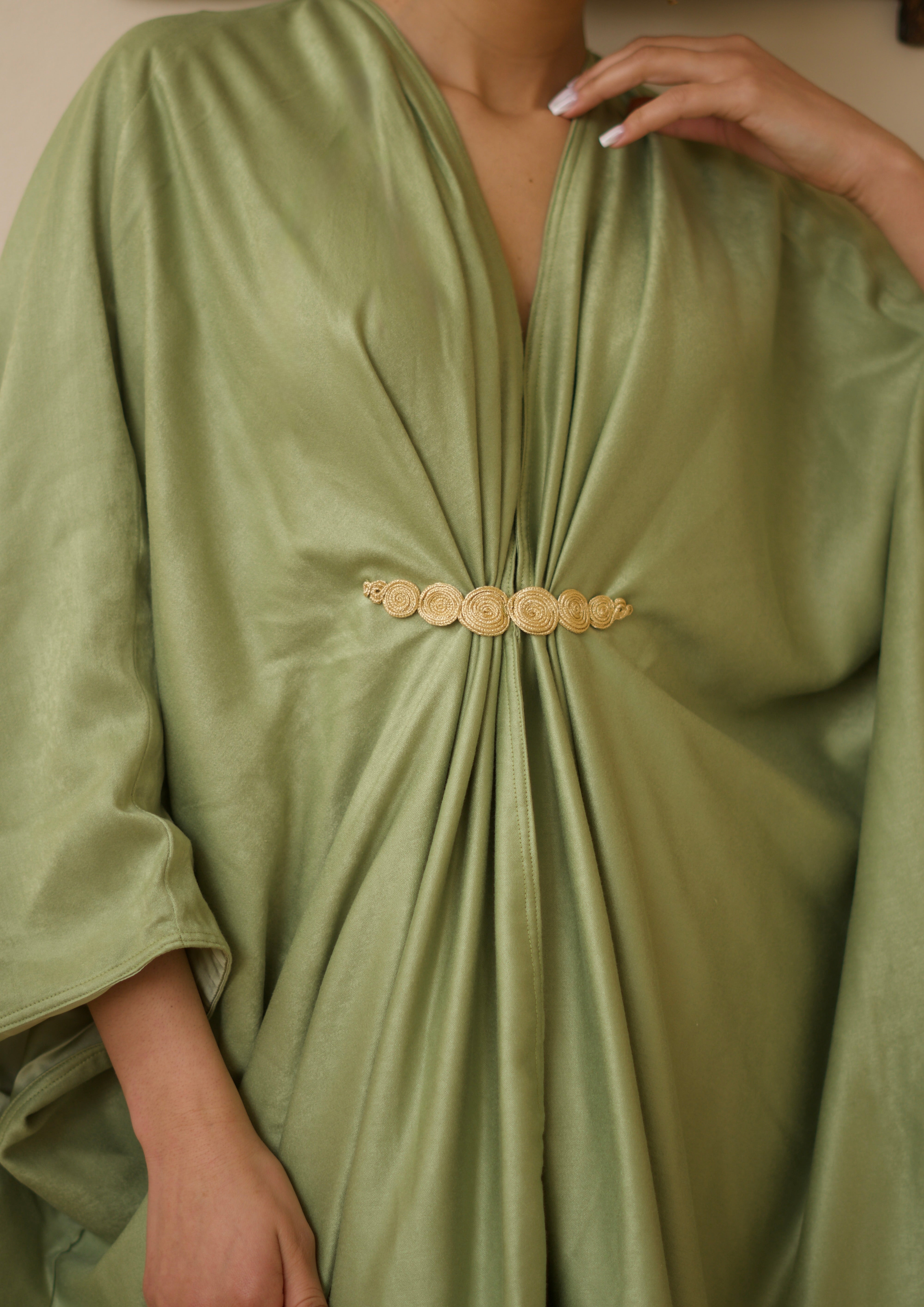 Gros plan sur la broche marocaine ornant une robe longue en soie mlifa verte.