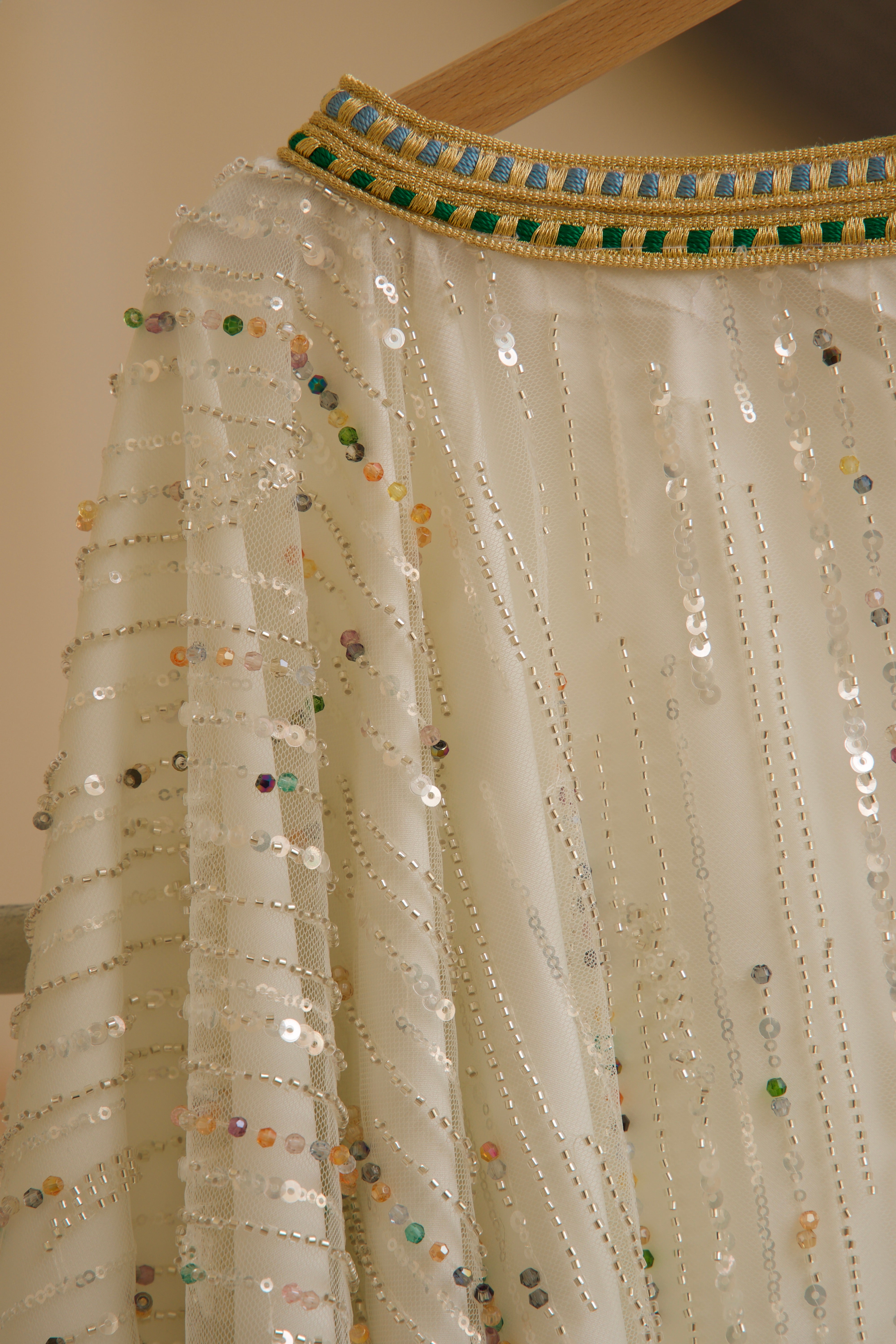Close-up of multicolored beads and sequins sewn onto a white tulle cape.