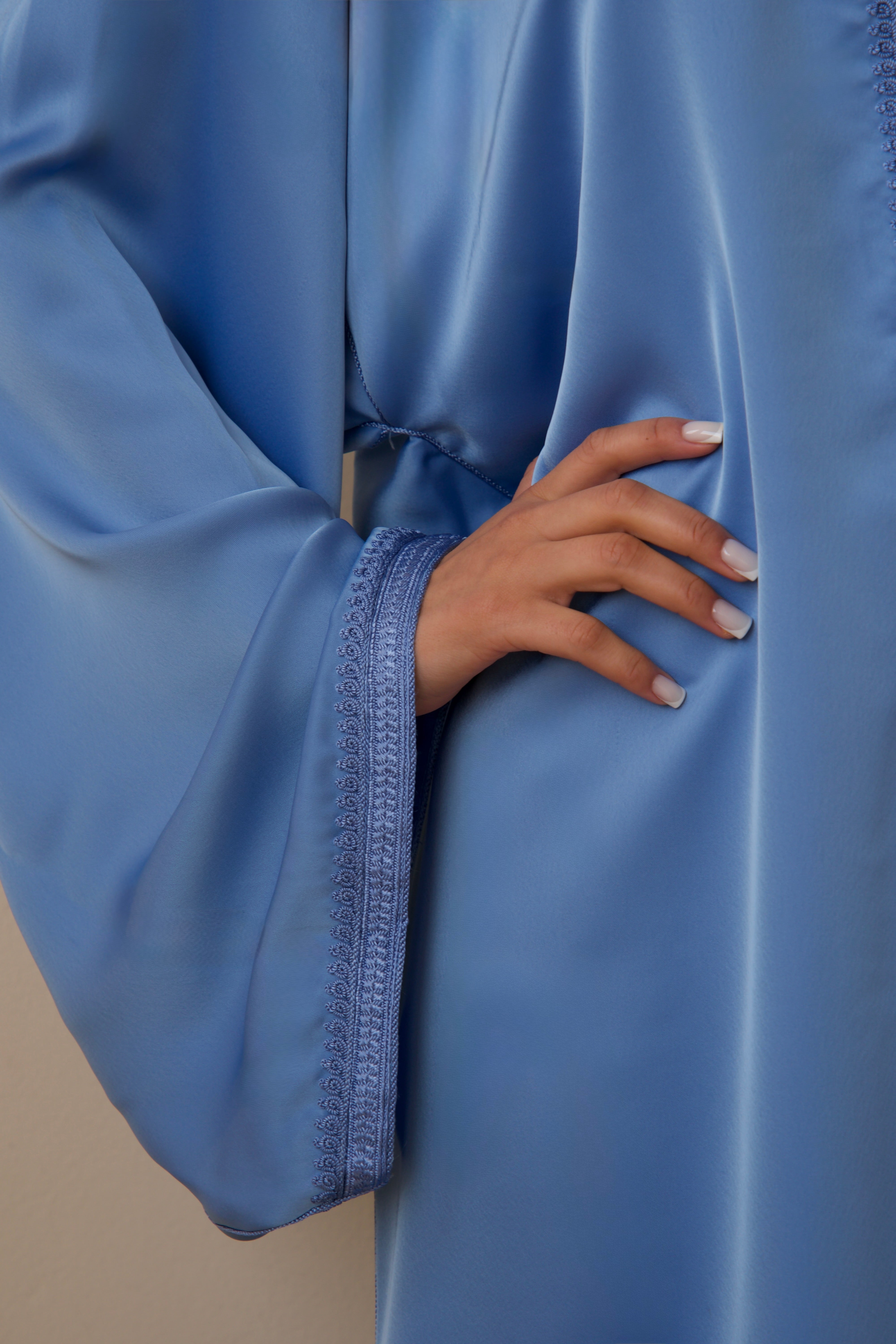 Gros plan sur la manche brodée ornée de sfifa d’une jellaba en satin duchesse bleu.