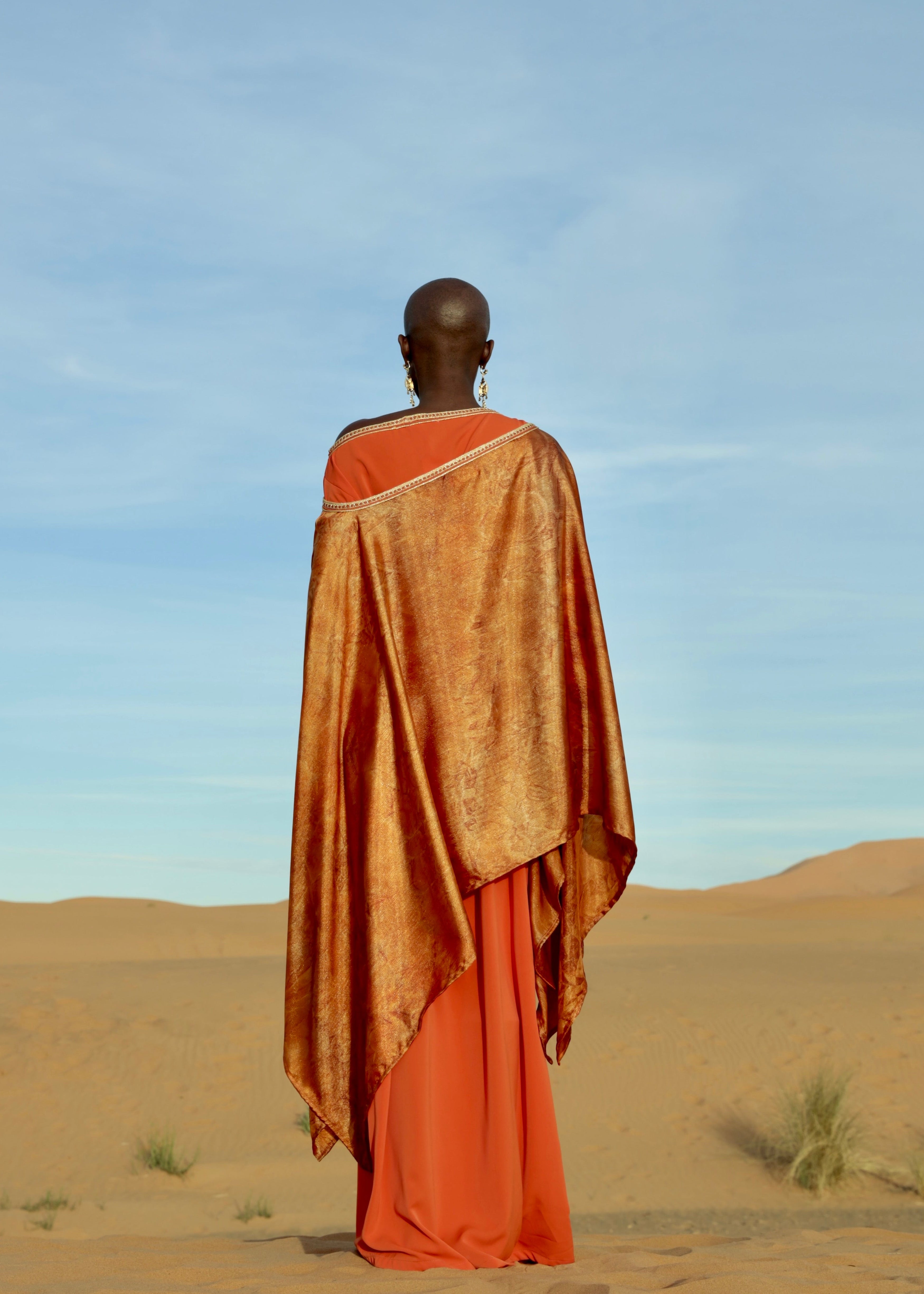 An orange cape with a printed design on the back, made of lamé silk, highlighting the fabric's lightness and shimmer.