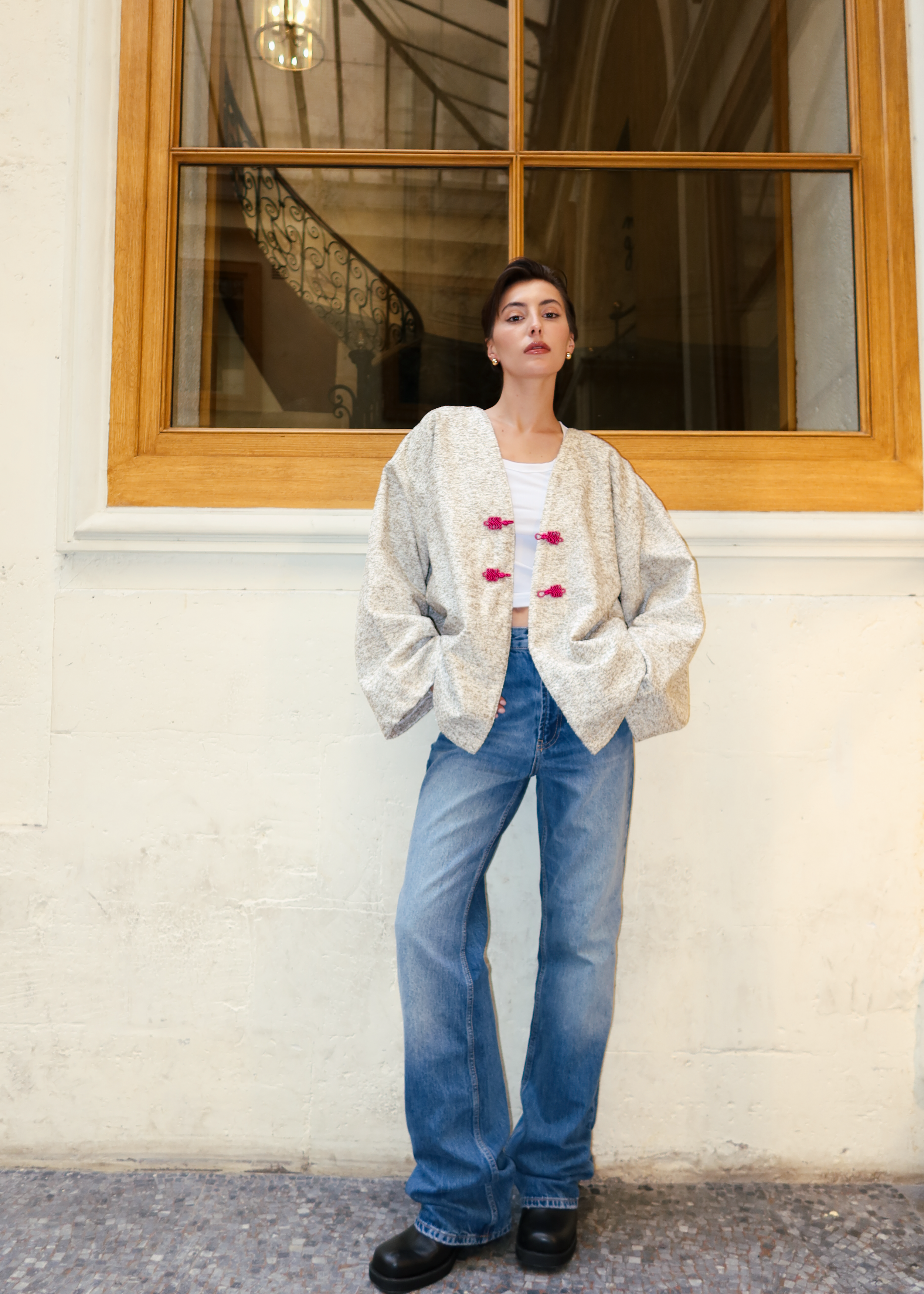 Veste en laine bouclée vert et beige photographiée en plein pied, avec boutons marocains roses et style chic