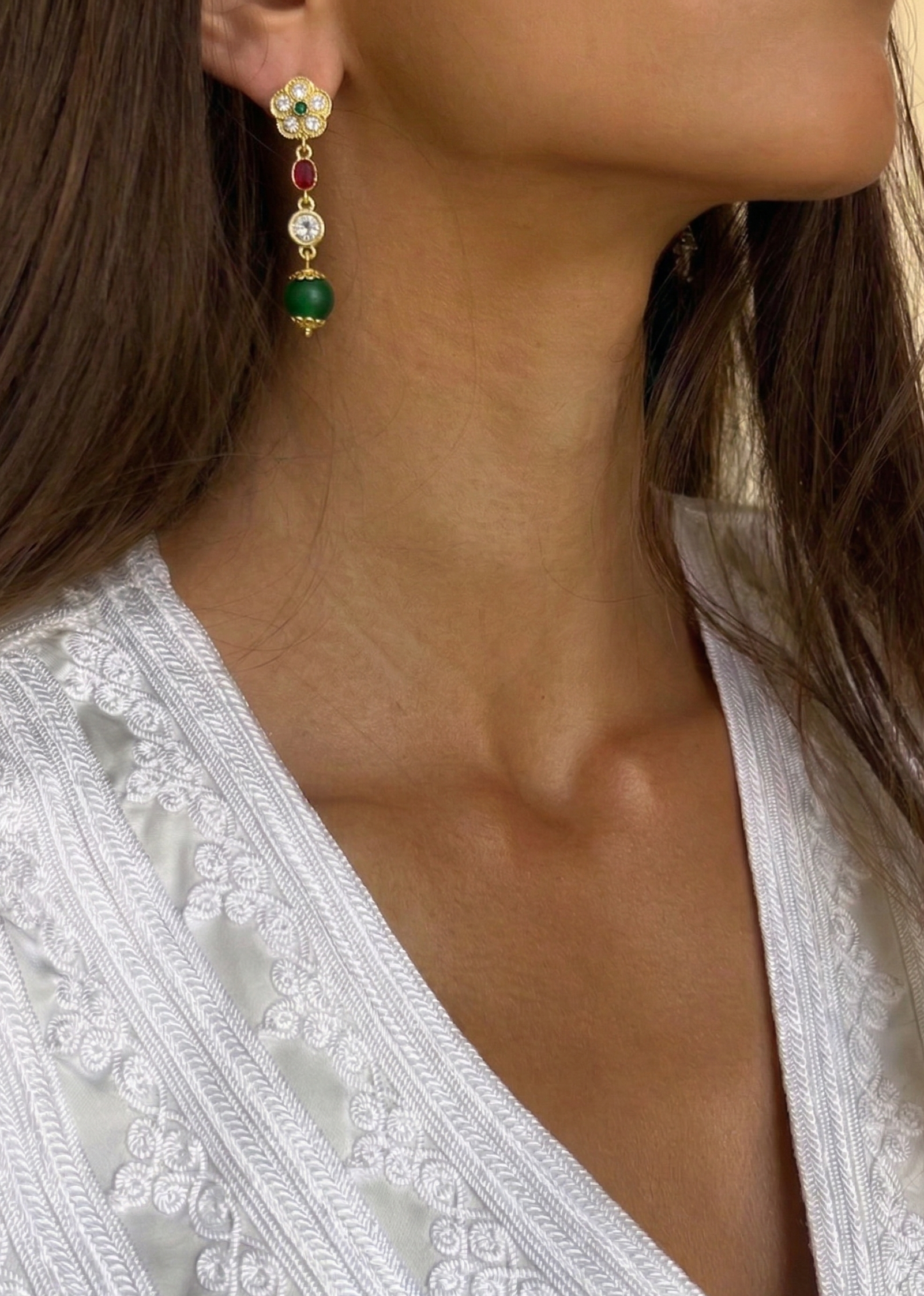 Photo portée des boucles d’oreilles à pierres rouges et vertes avec finition dorée