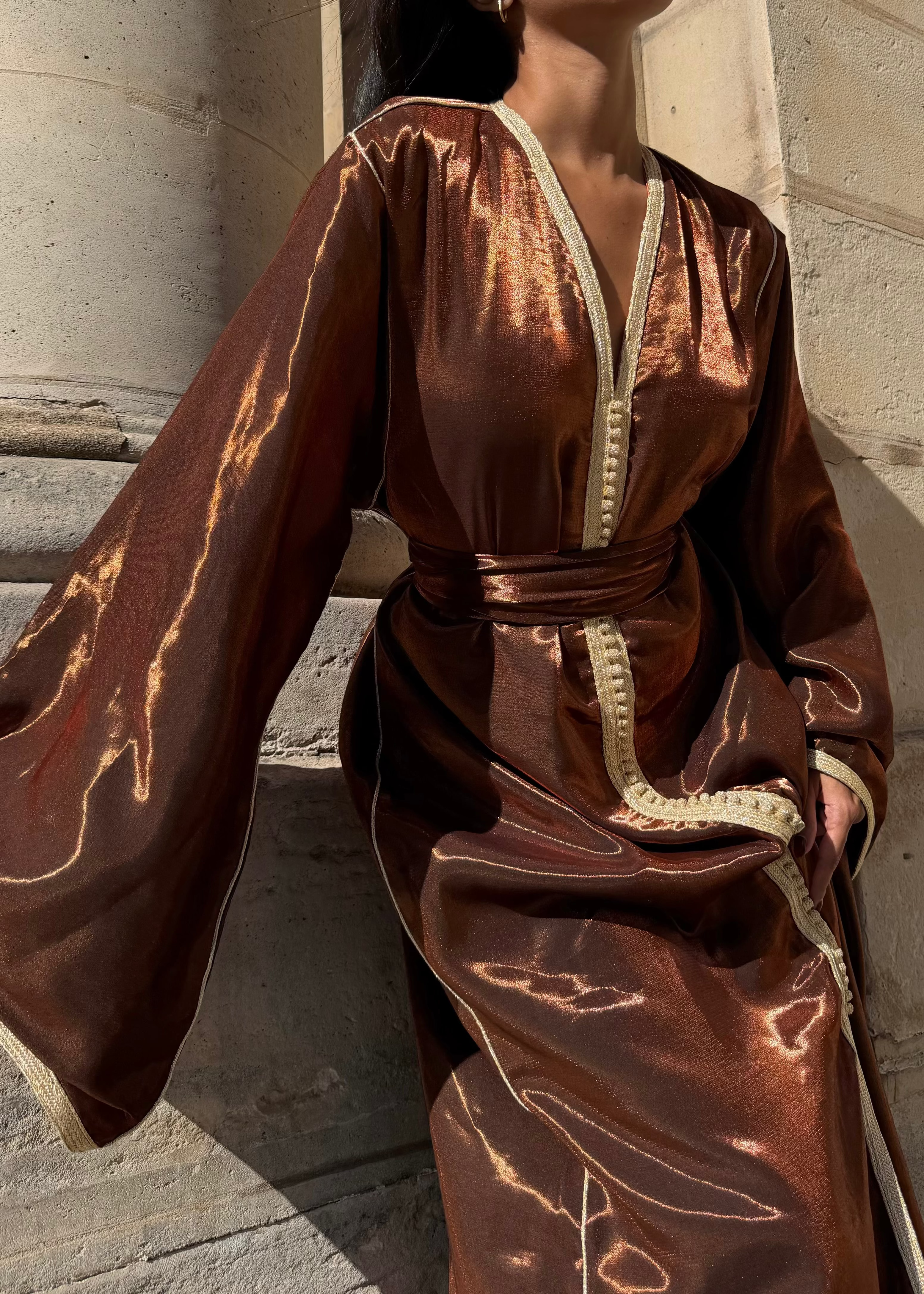 Gros plan sur la texture satinée marron effet bronze du caftan, mettant en valeur les reflets métalliques.