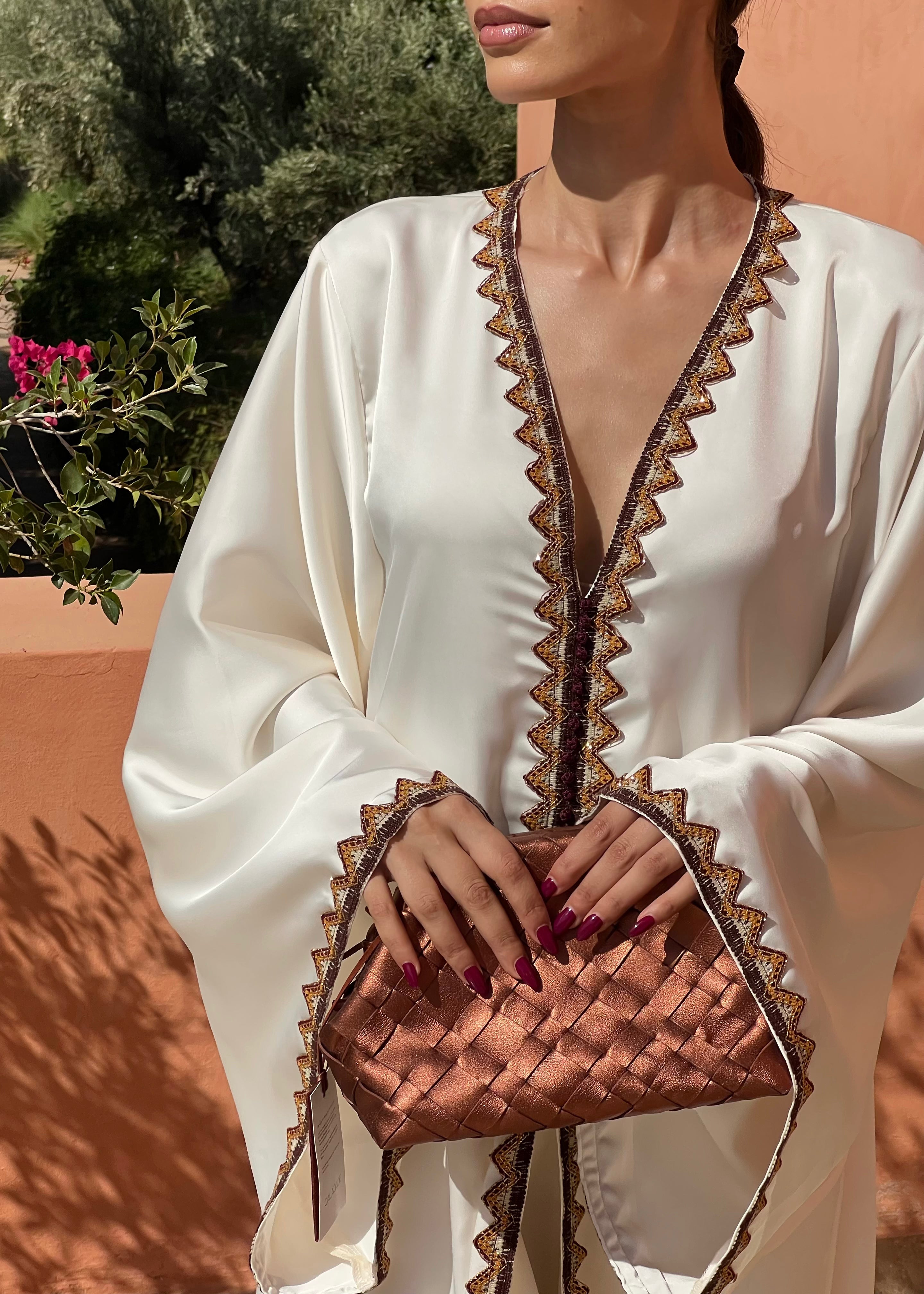 Détail de la broderie kabyle marron et orange sur drap de soie blanc, couture artisanale et motifs berbères raffinés