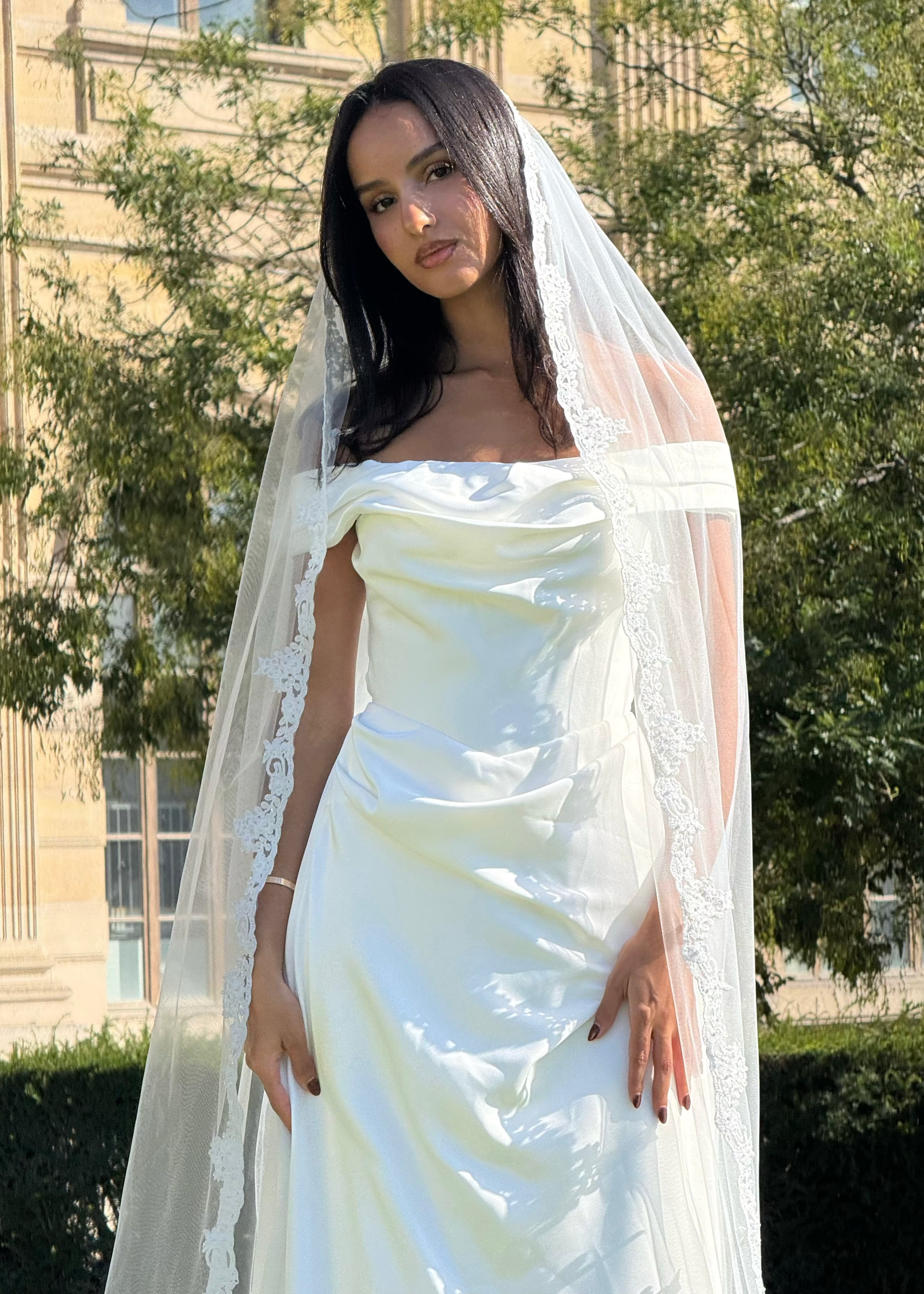 Vue de face d’une mariée portant un voile long avec bordure en dentelle florale délicate.
