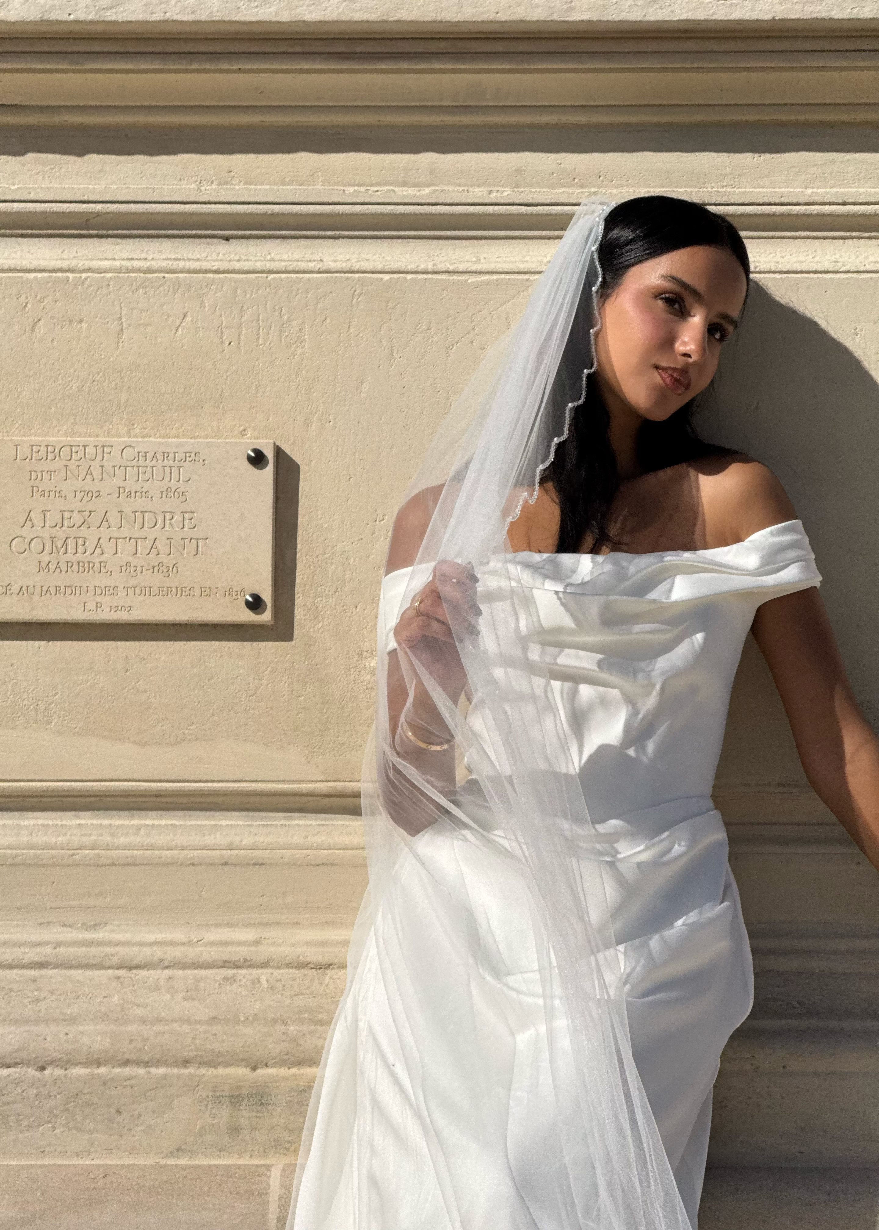 Vue de face d’une mariée portant un voile long avec une bordure perlée au motif ondulé.
