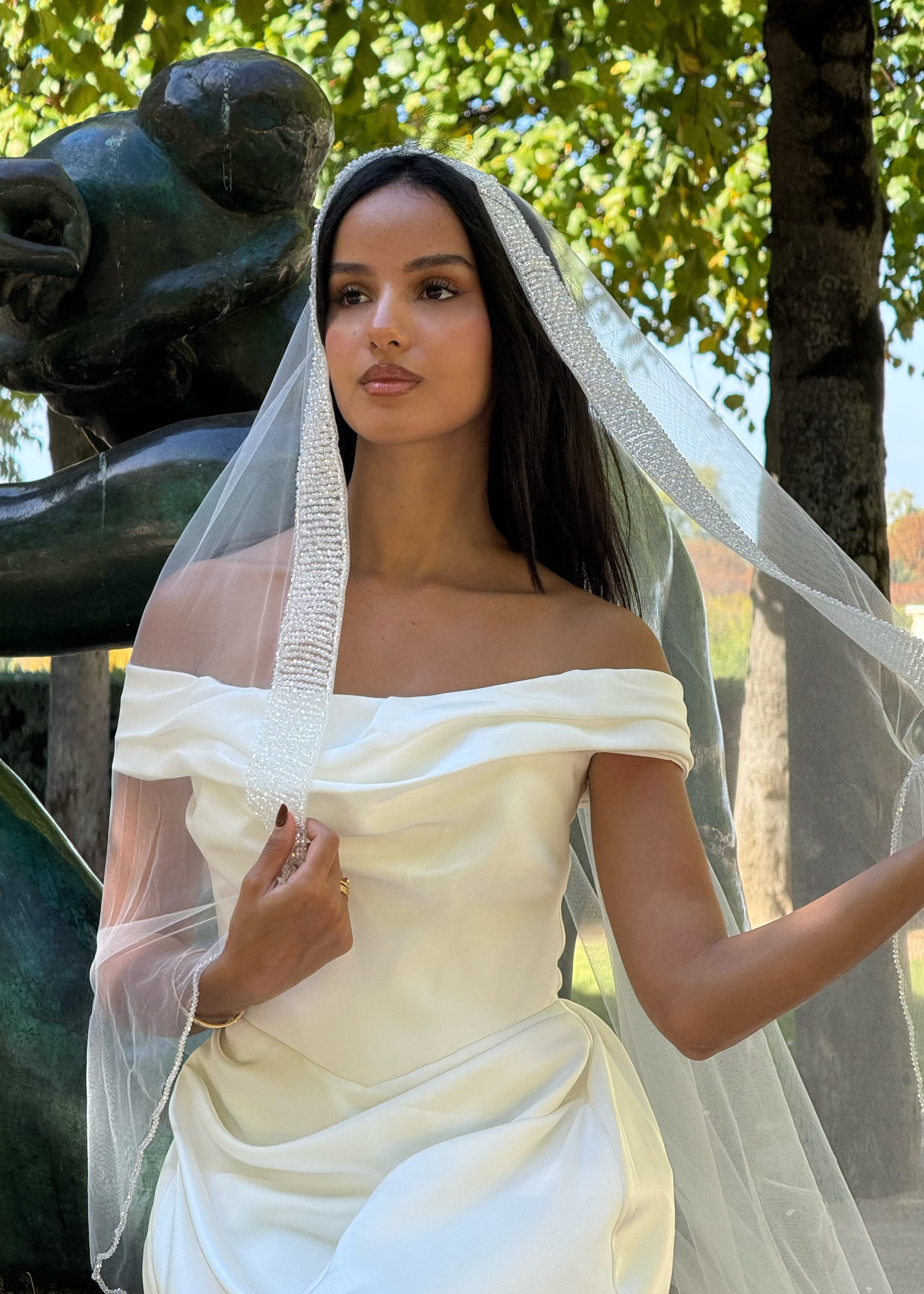 Vue de face d’une mariée portant un voile long perlé avec une bordure scintillante élégante.