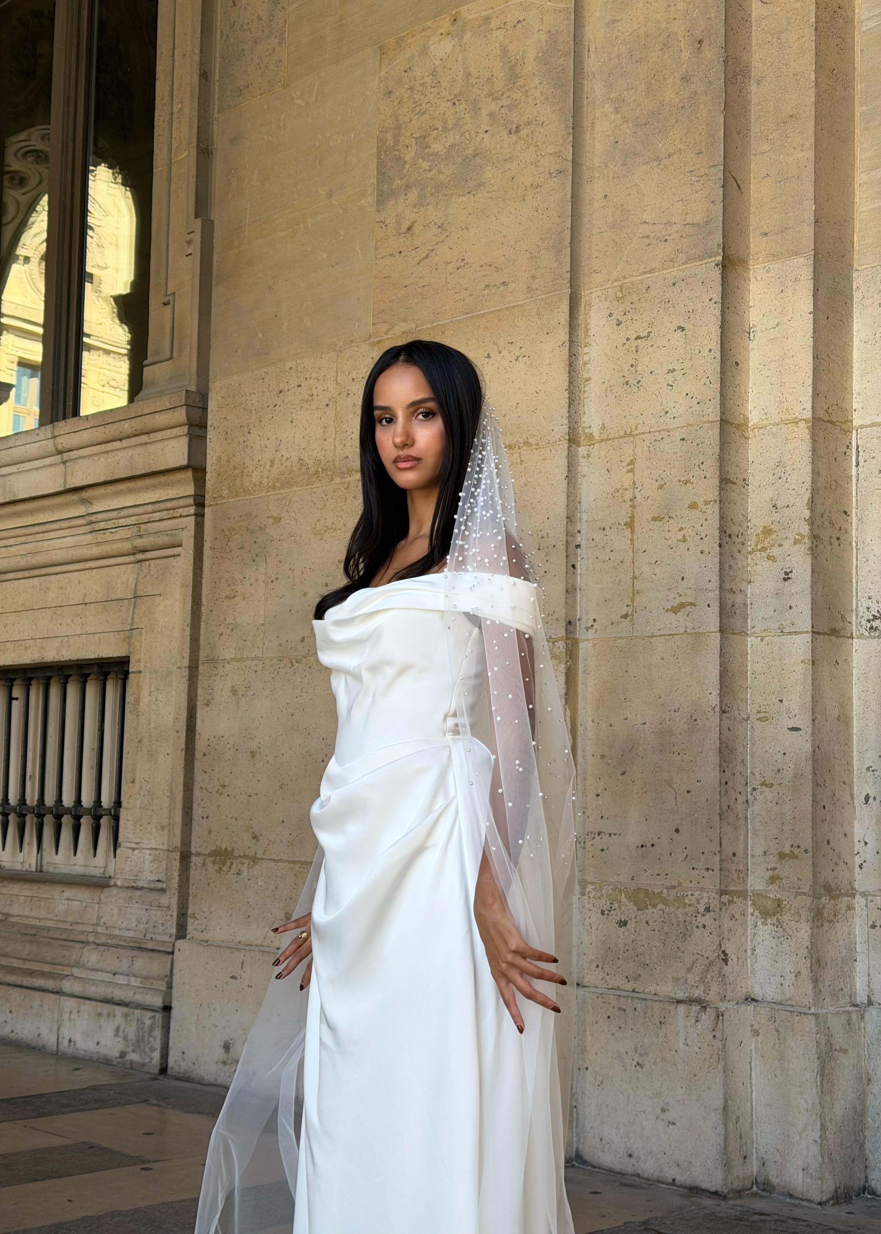 Vue de face d’une mariée portant un voile long en tulle orné de perles brodées délicatement.