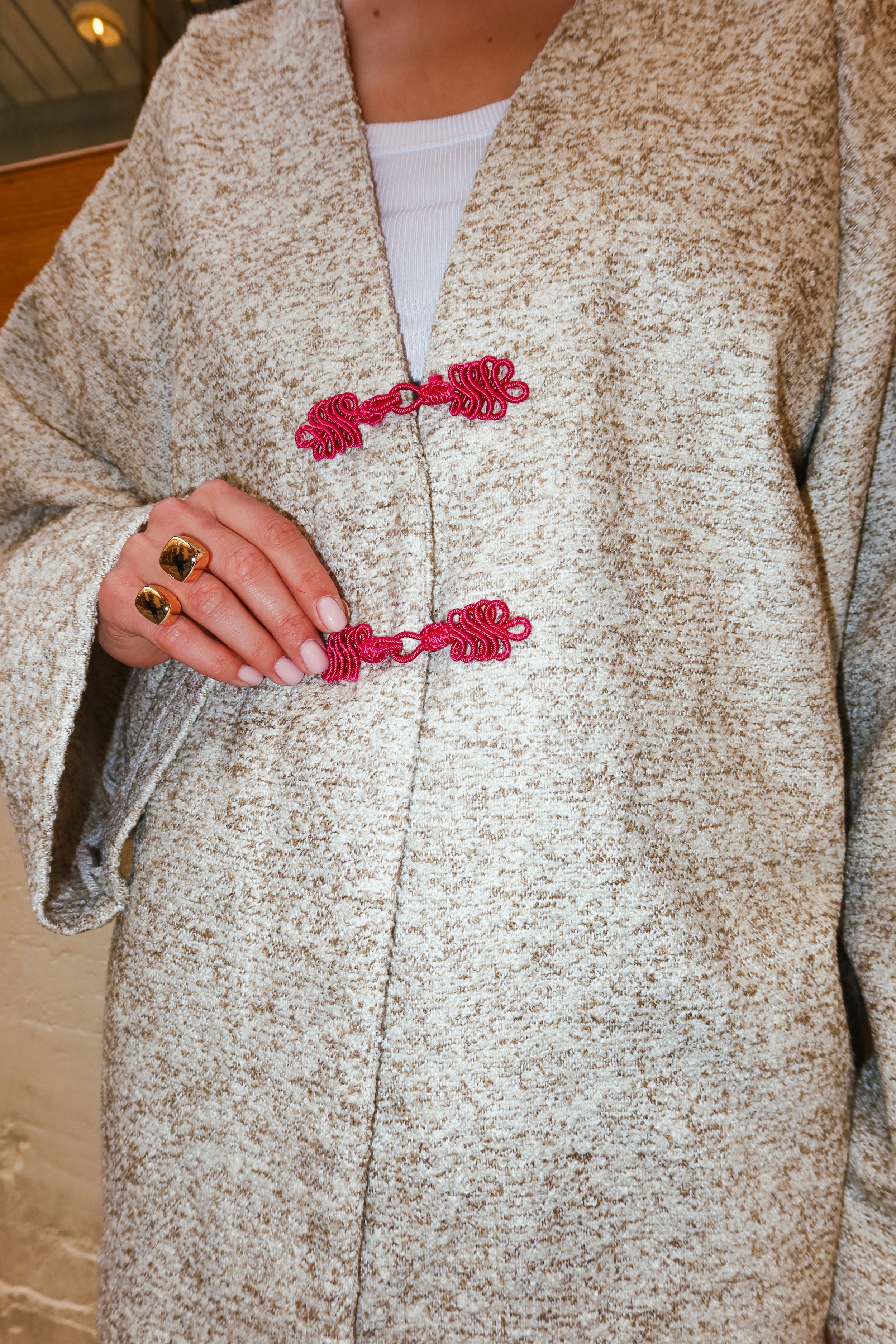 Close-up of handmade pink Moroccan buttons on a green and beige bouclé wool jacket