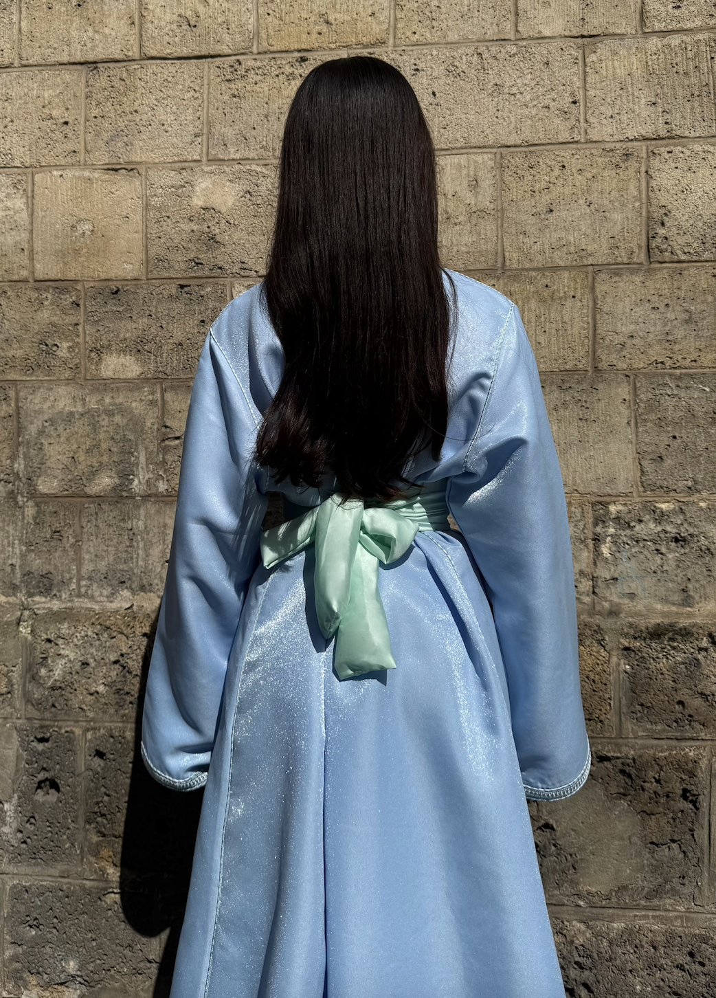 Kaftan in blue satin seen from the back, highlighting the fluidity of the fabric and the finesse of the finishing touches.