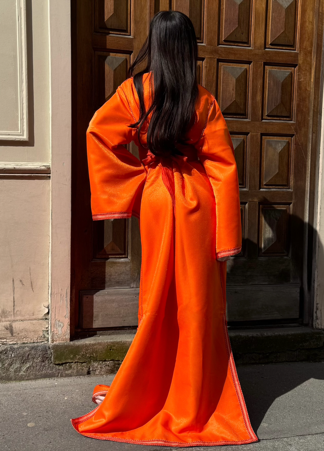 Orange satin Kaftan seen from the back, highlighting the fluidity of the satin and the finesse of the finishing touches.