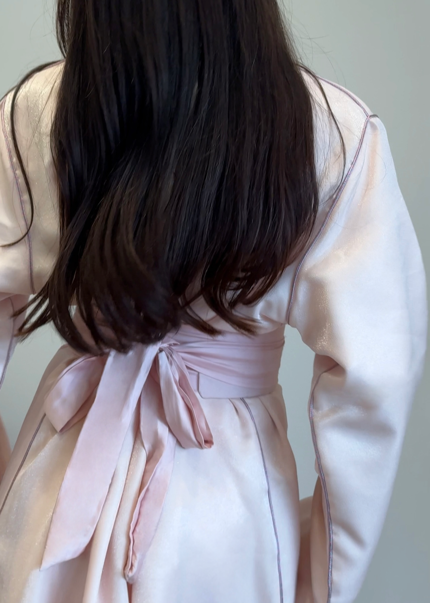 Pink satin Kaftan seen from the back, revealing the fluidity of the fabric and the finesse of the finishing touches.