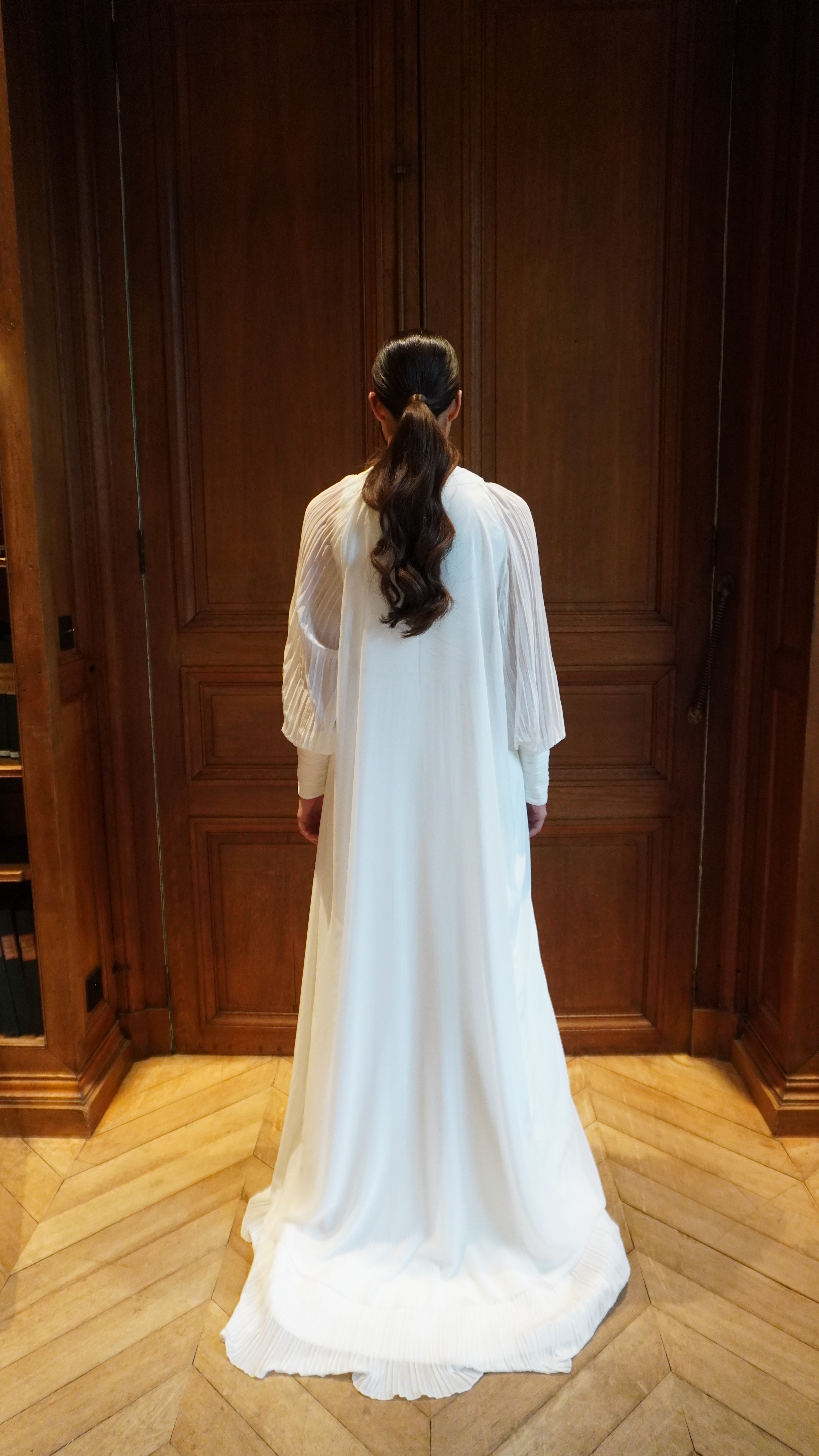 Back view of the pleated wedding cape in light tulle, with a fluid and transparent drape