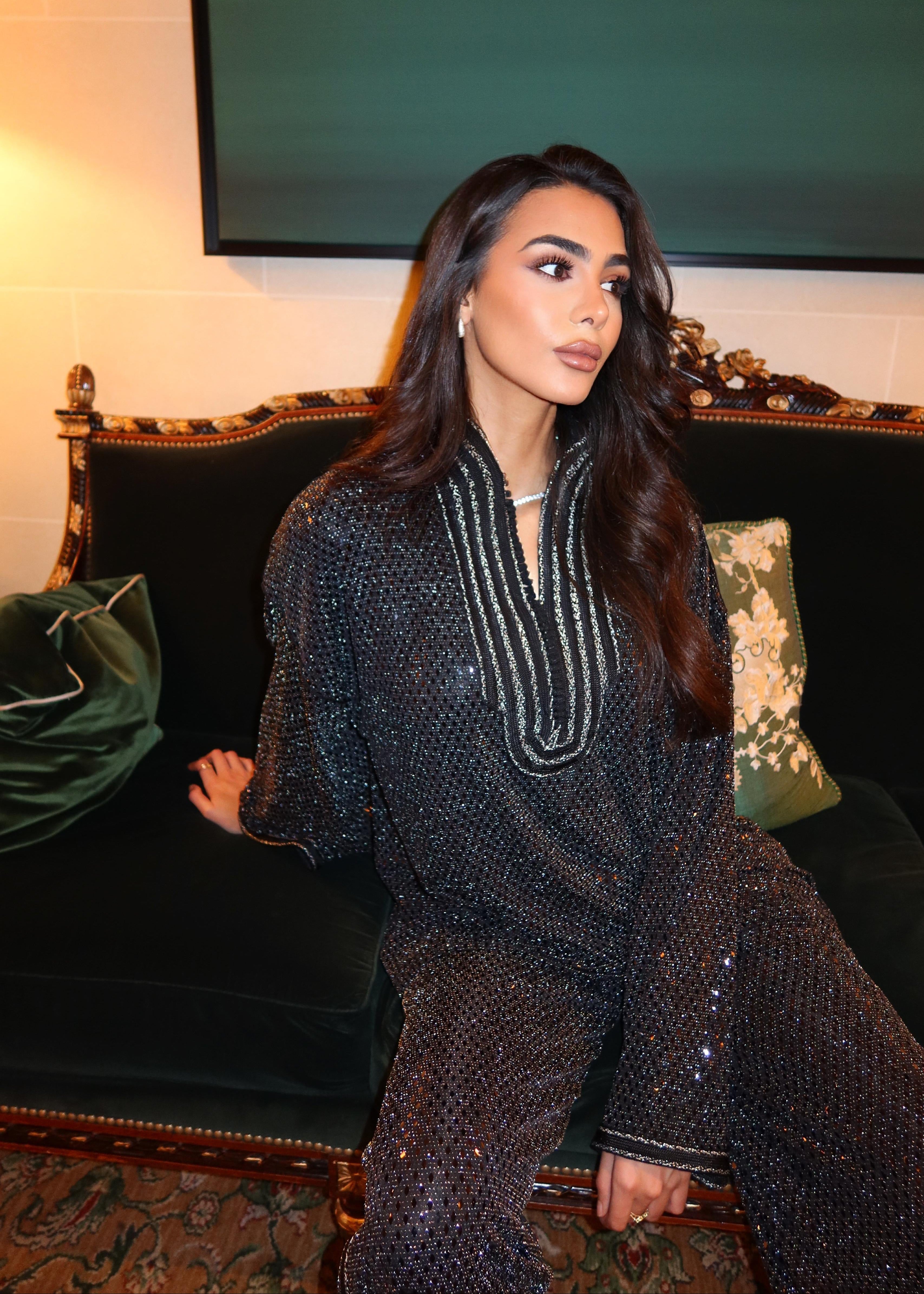Seated profile photo of the shimmering black jacquard ensemble adorned with sfifa, hand-crafted finishes and the fluid fall of the shiny fabric.