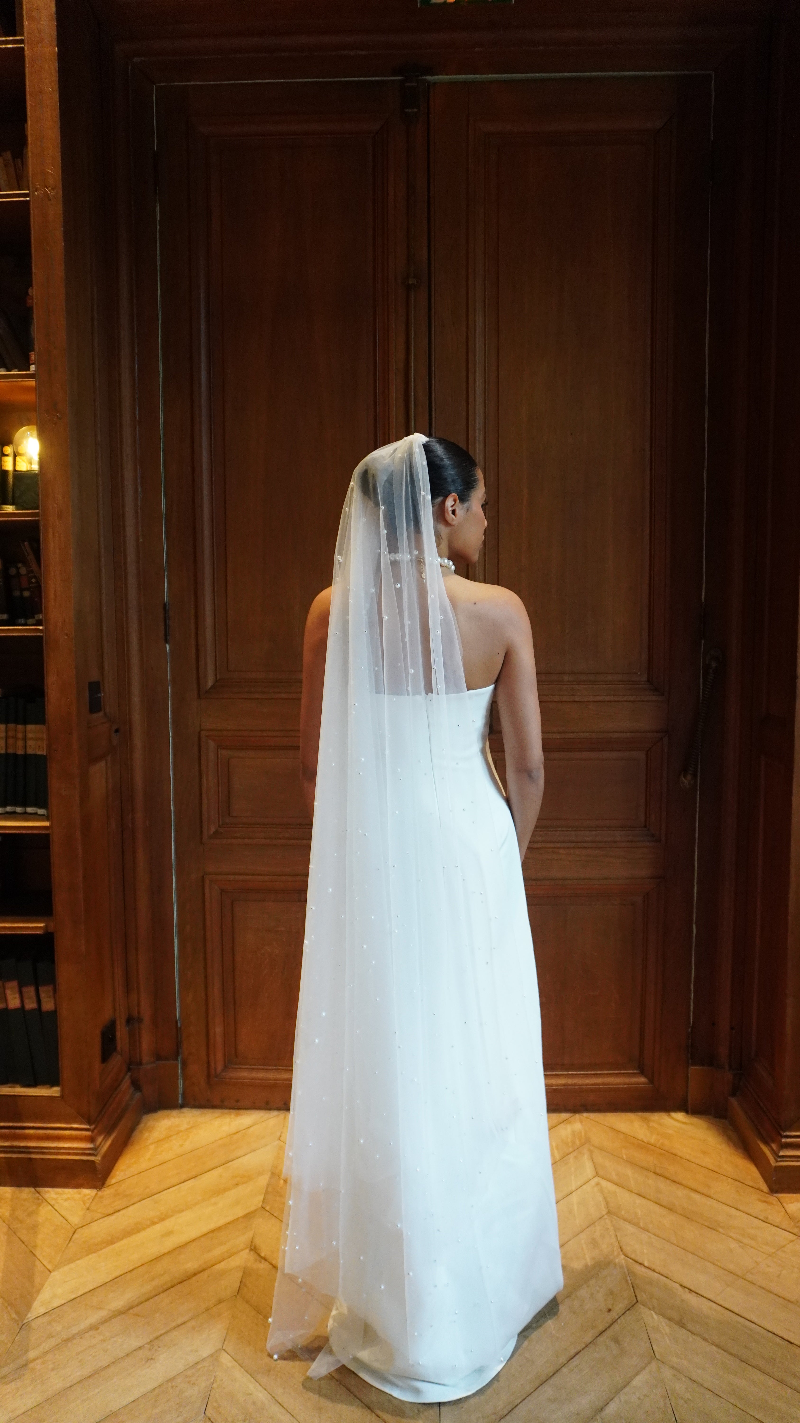 Strapless straight wedding dress seen from the back, revealing a light, flowing train and refined lines.