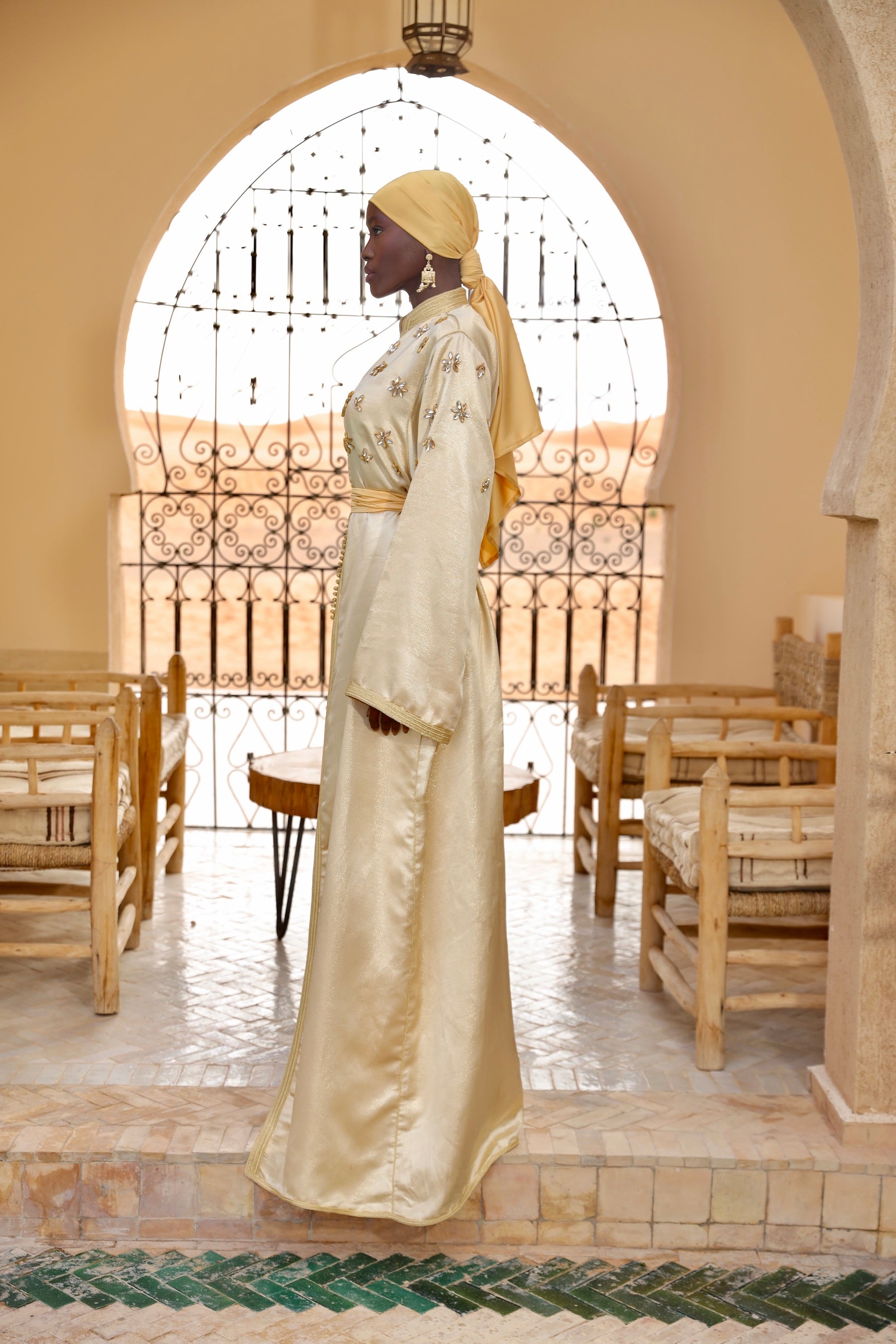 Caftan en soie lamée dorée ornée de perles, porté de profil.