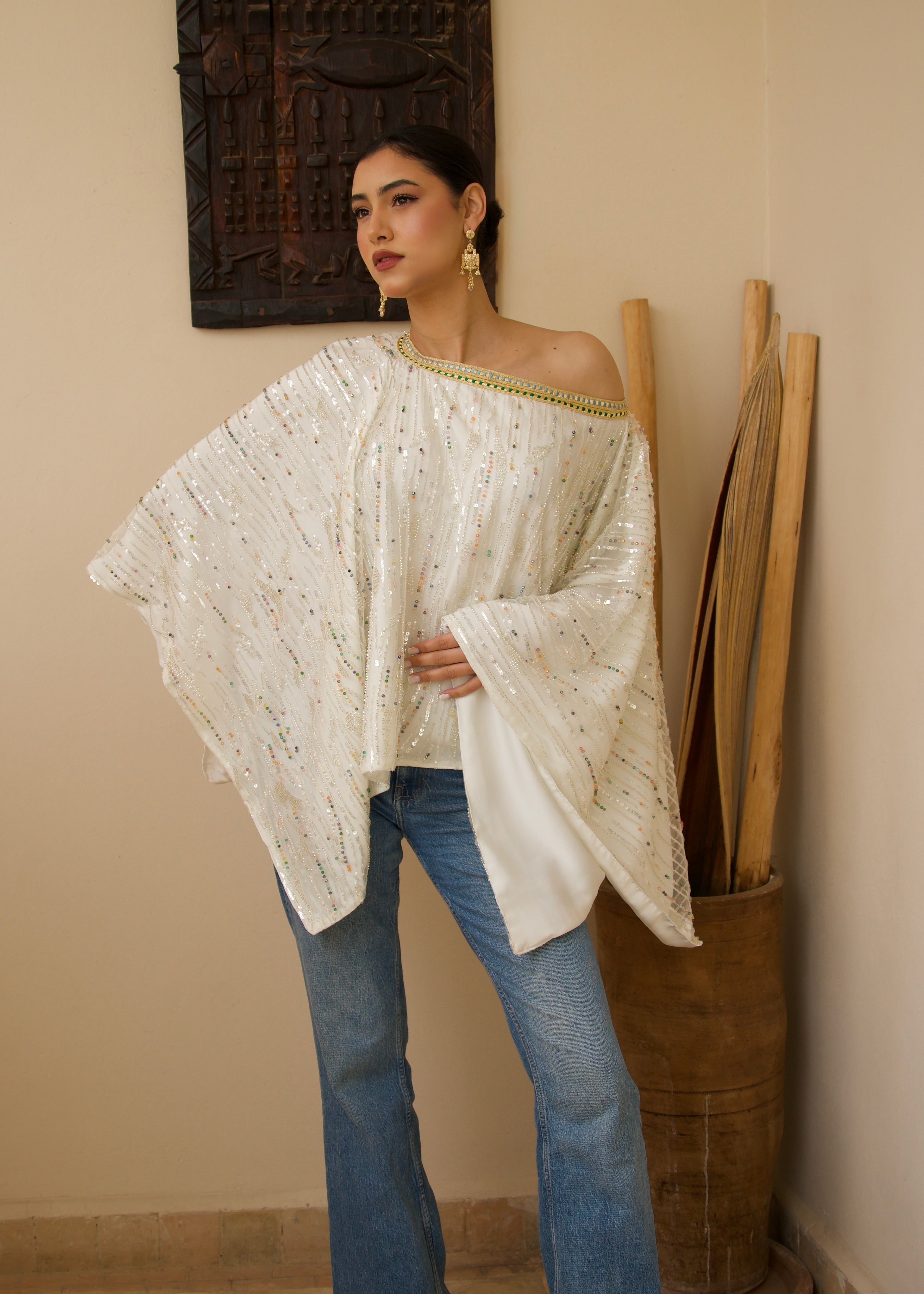 White cape in transparent tulle decorated with multicolored pearls, seen from the front.