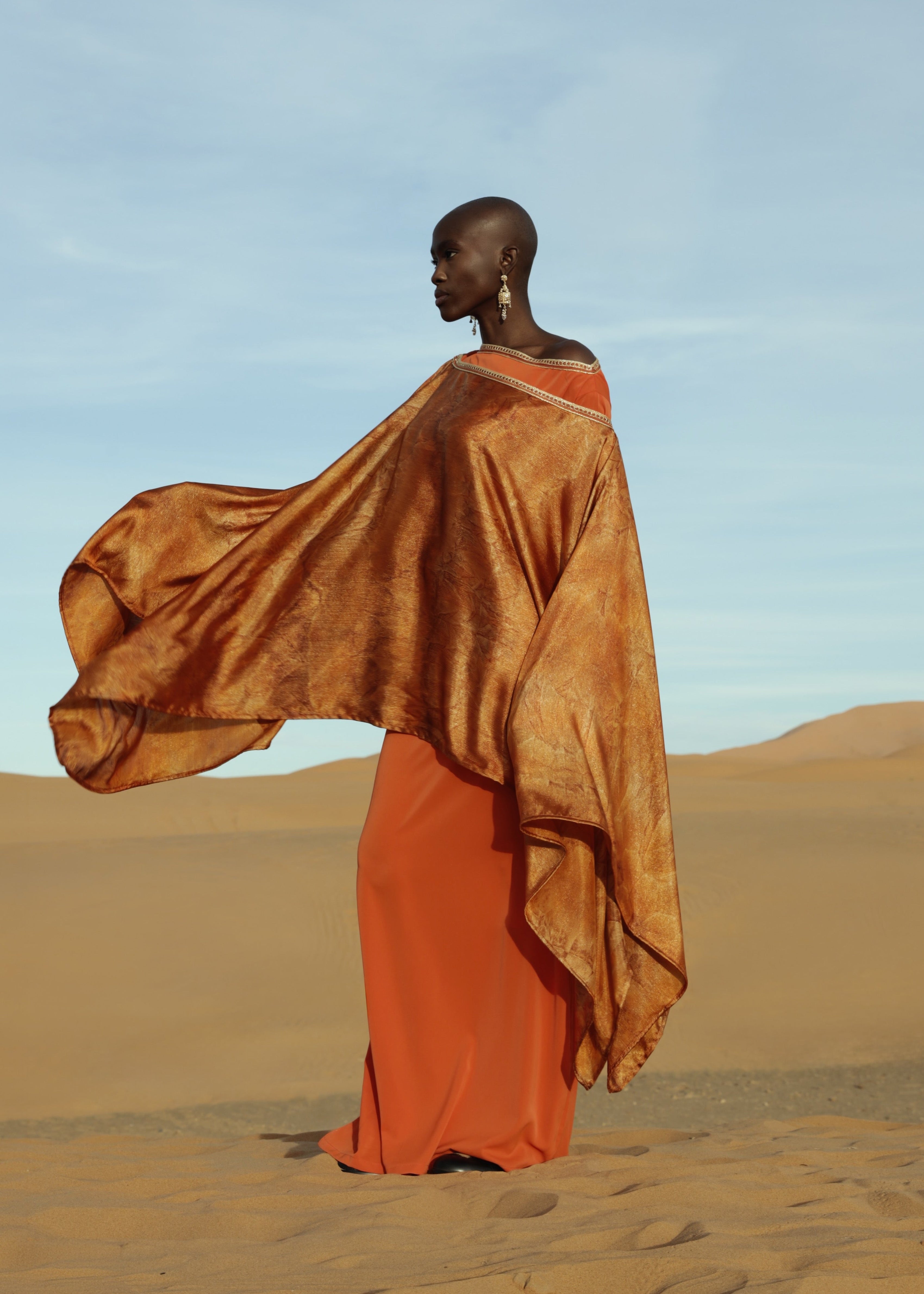 An orange printed cape made of lamé silk, designed to flow with movement, creating a fluid and elegant look.