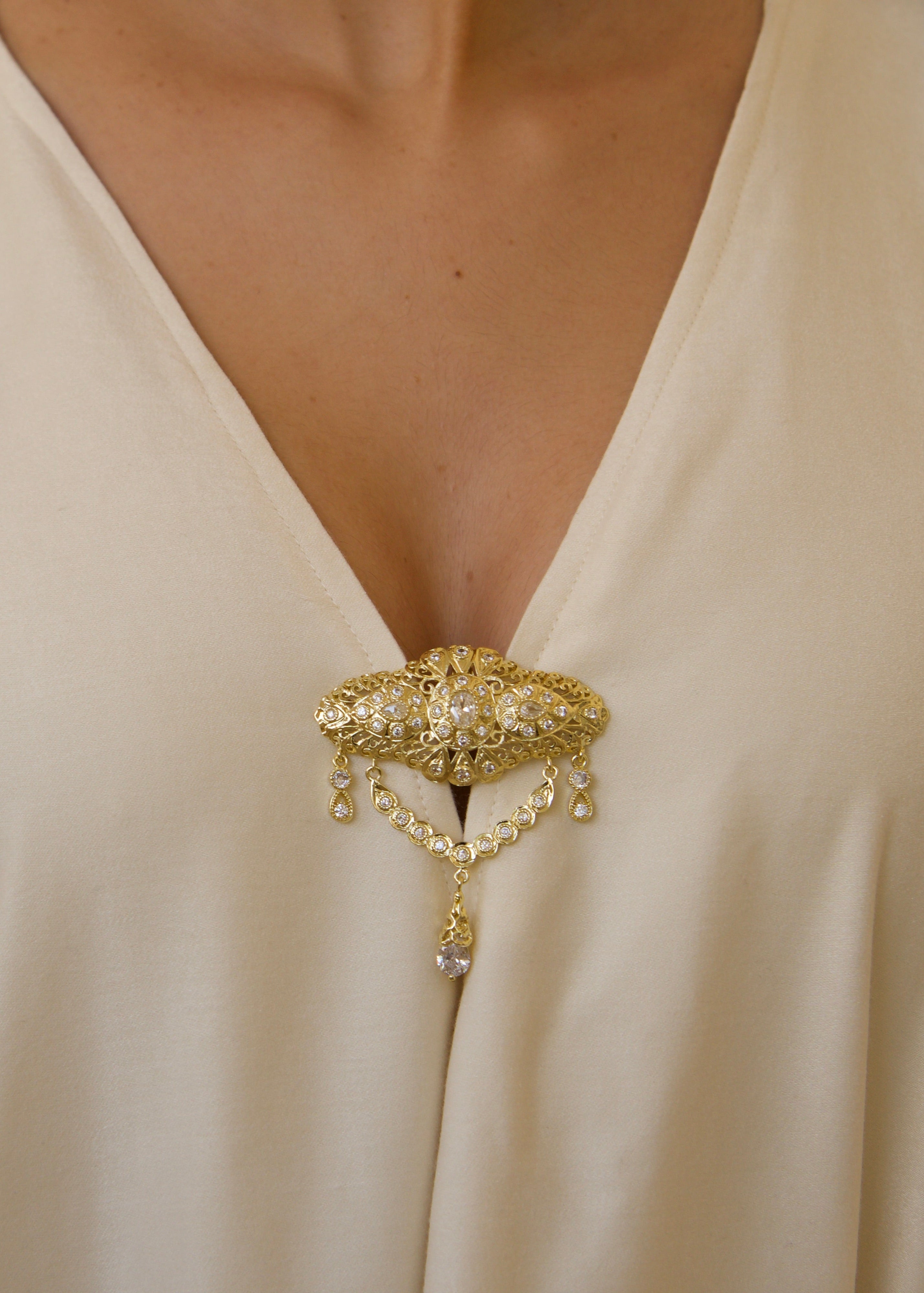 Gros plan sur la broche marocaine ornant une robe longue en soie mlifa blanche.