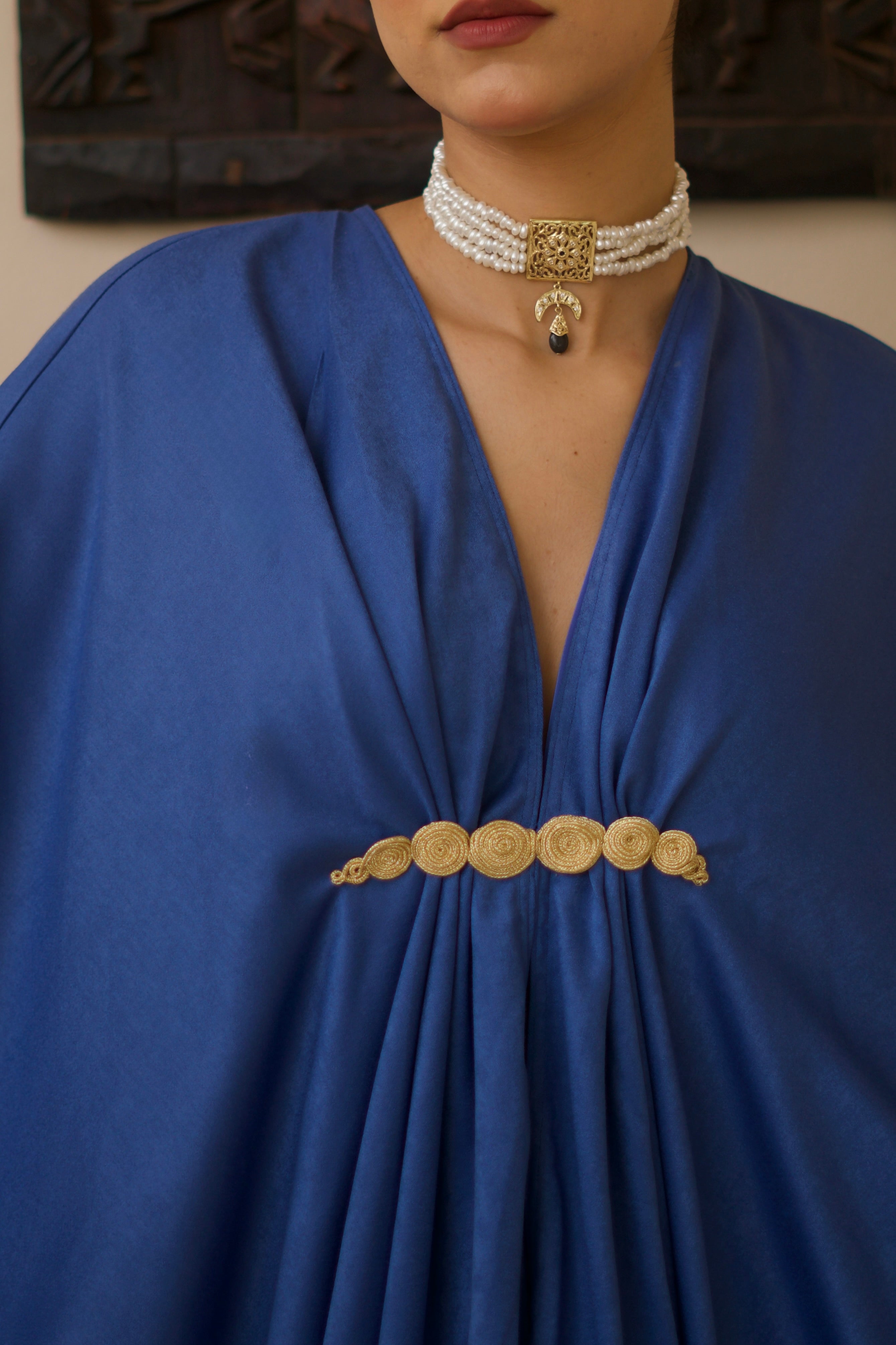 Gros plan sur la broche marocaine ornant une robe longue en soie mlifa bleue.
