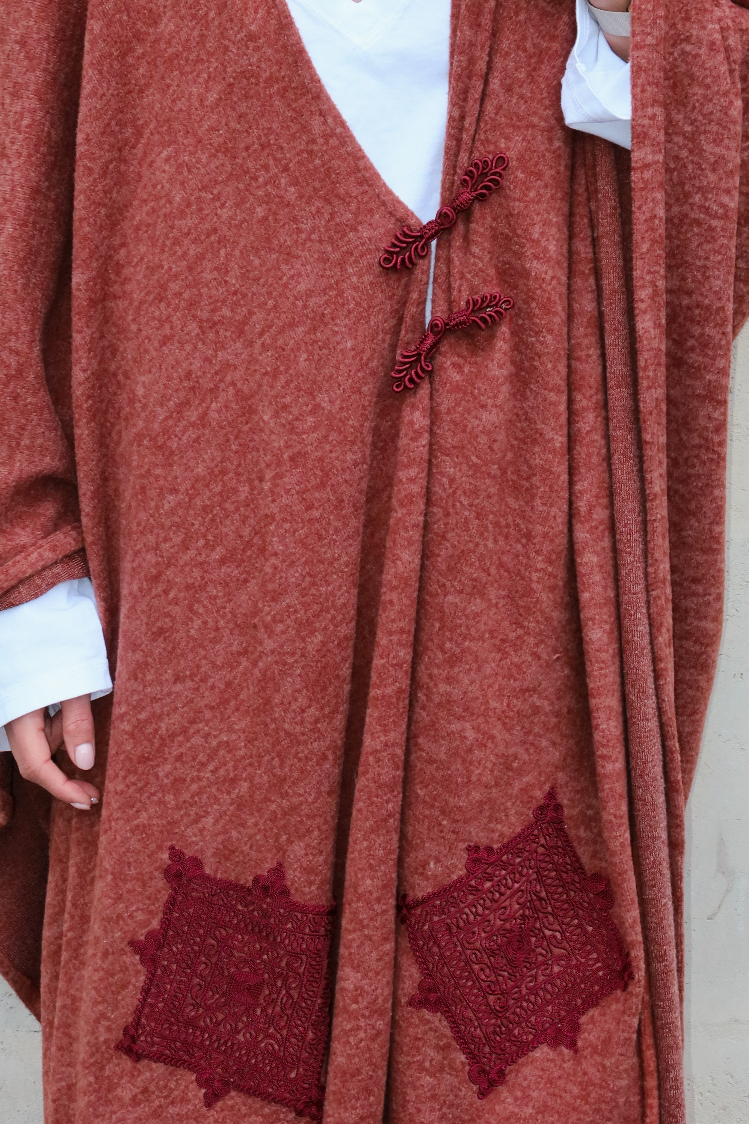Gros plan sur les broderies et crochets marocains et la texture de la laine d’un gilet bohème long couleur bordeaux