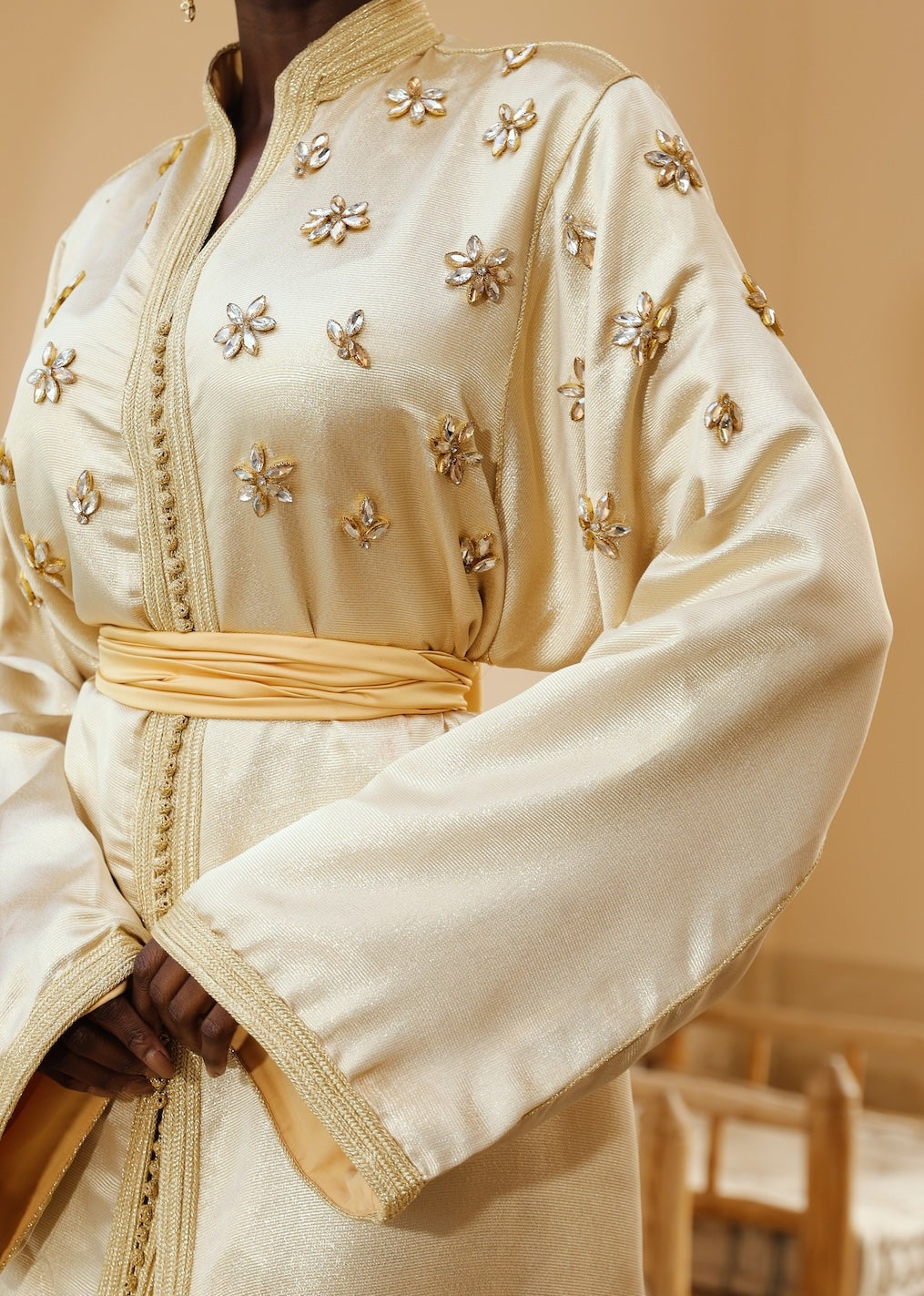 Gros plan sur les perles brodées d’un caftan en soie lamée dorée.