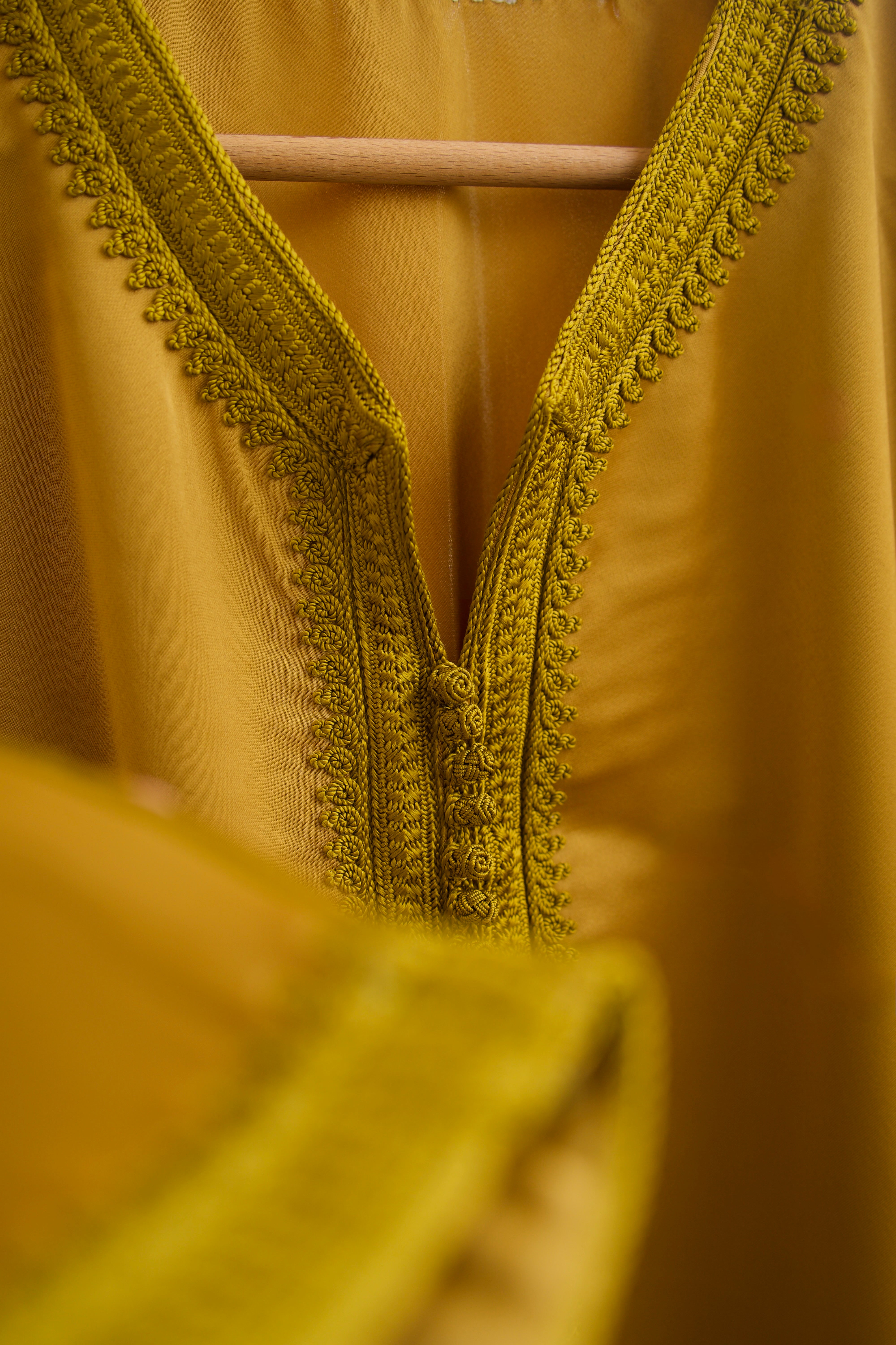 Gros plan sur la sfifa artisanale d’une jellaba en satin duchesse moutarde.