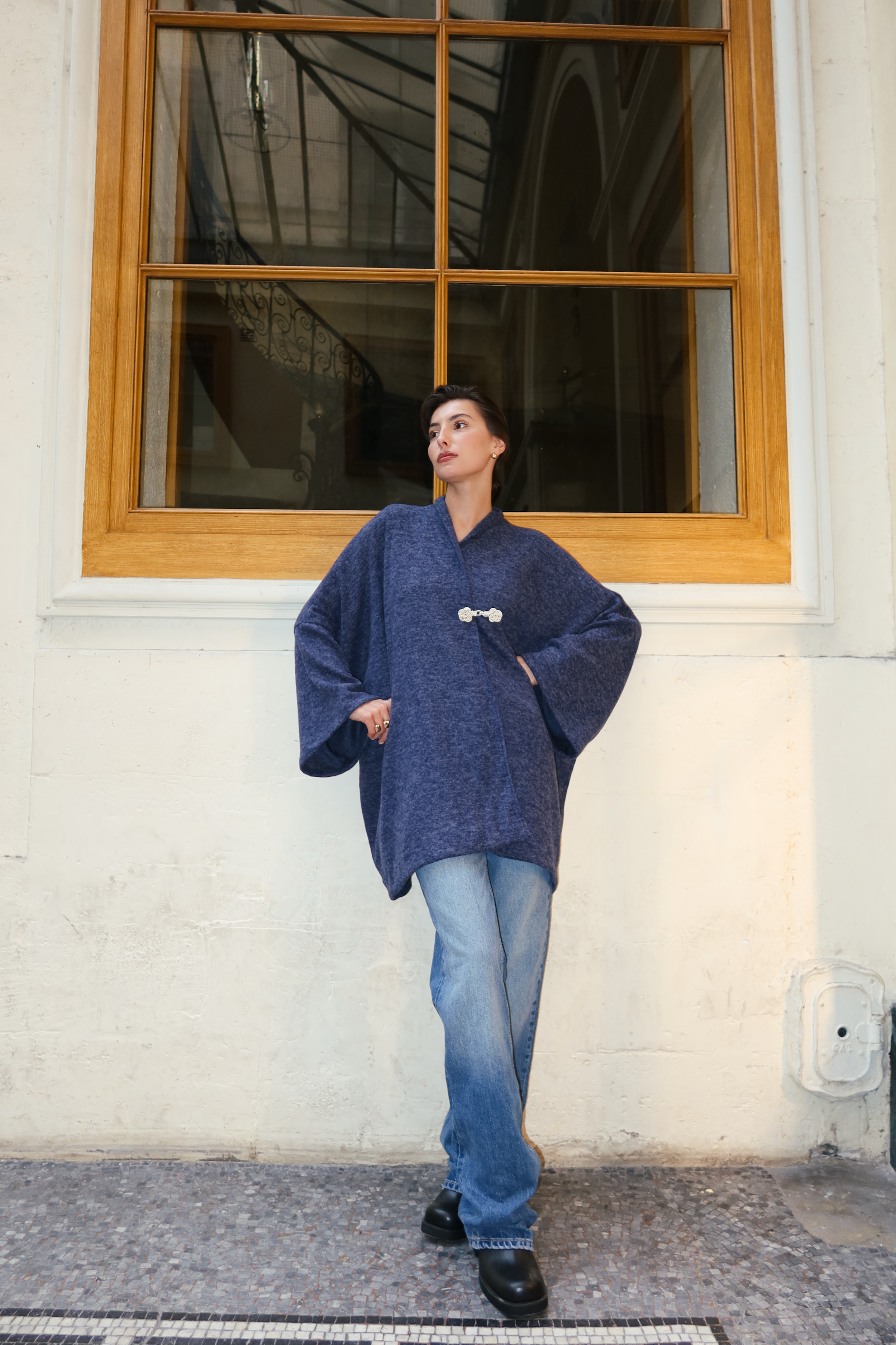 Gilet en laine bleu photographié en plein pied, avec fermeture à crochet et style chic