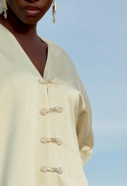 Gros plan sur les crochets blancs décoratifs d’une robe en satin plissé blanc.