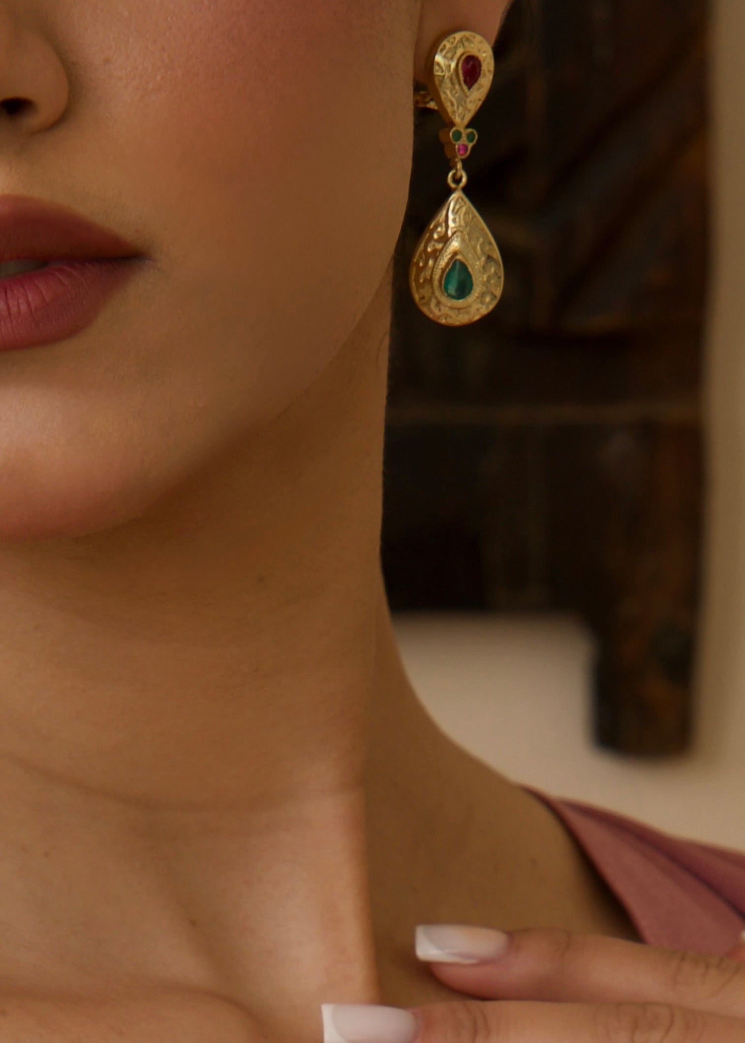 Détail boucles d'oreilles dorées avec pierres vertes et roses 