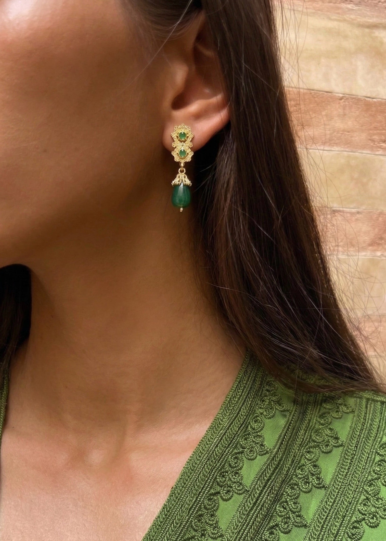 Gold earrings with green teardrop pendants worn with a Kaftan