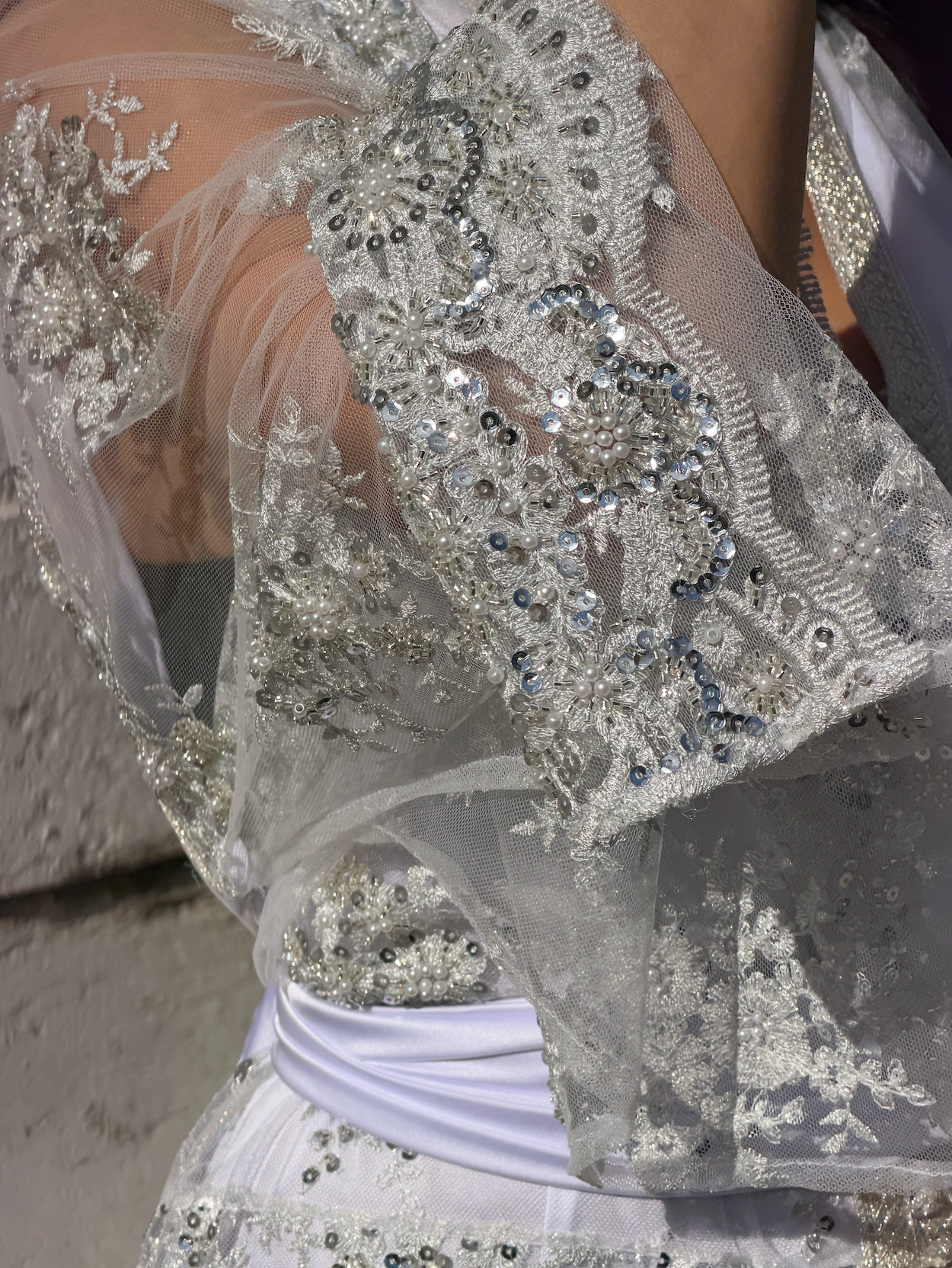 Détail de la manche en tulle brodé sur un caftan de mariée blanc orné de perles et d’ornements argentés
