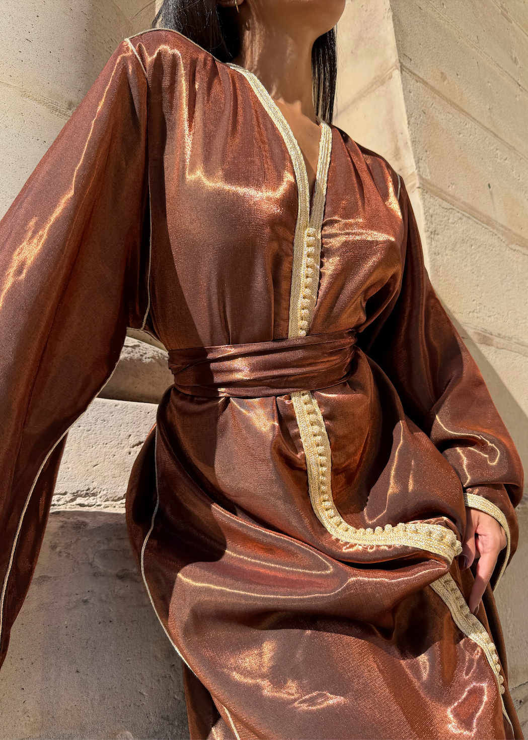 Photo lifestyle d’une femme portant le caftan en satin bronze dans un décor élégant.