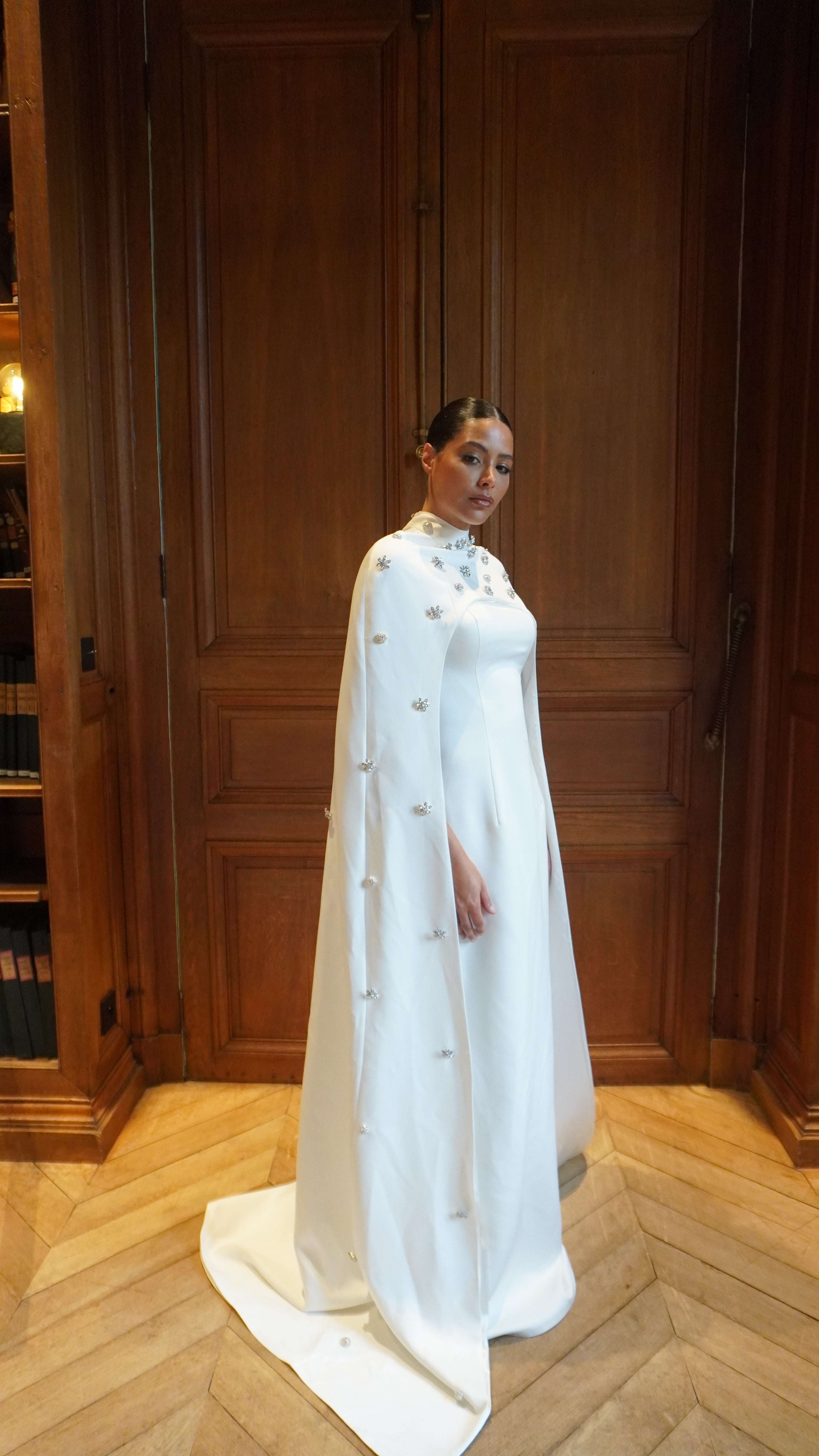 Cape de mariée en satin palace avec strass capturée en mouvement, soulignant la légèreté du satin et l’éclat des détails scintillants.