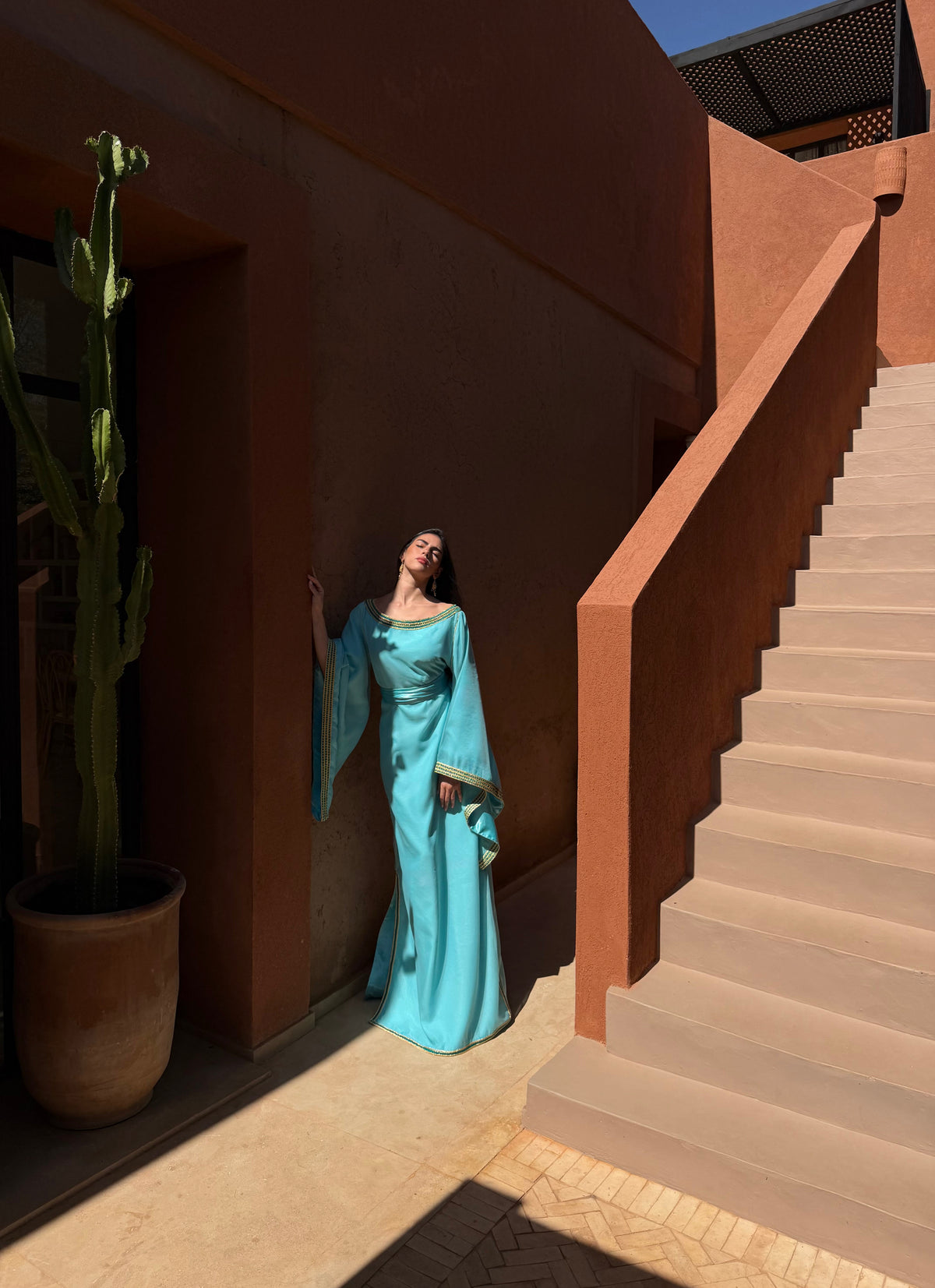 Robe Caftan Turquoise Clair à Col Bateau — Silhouette en pied près d’un escalier extérieur.
