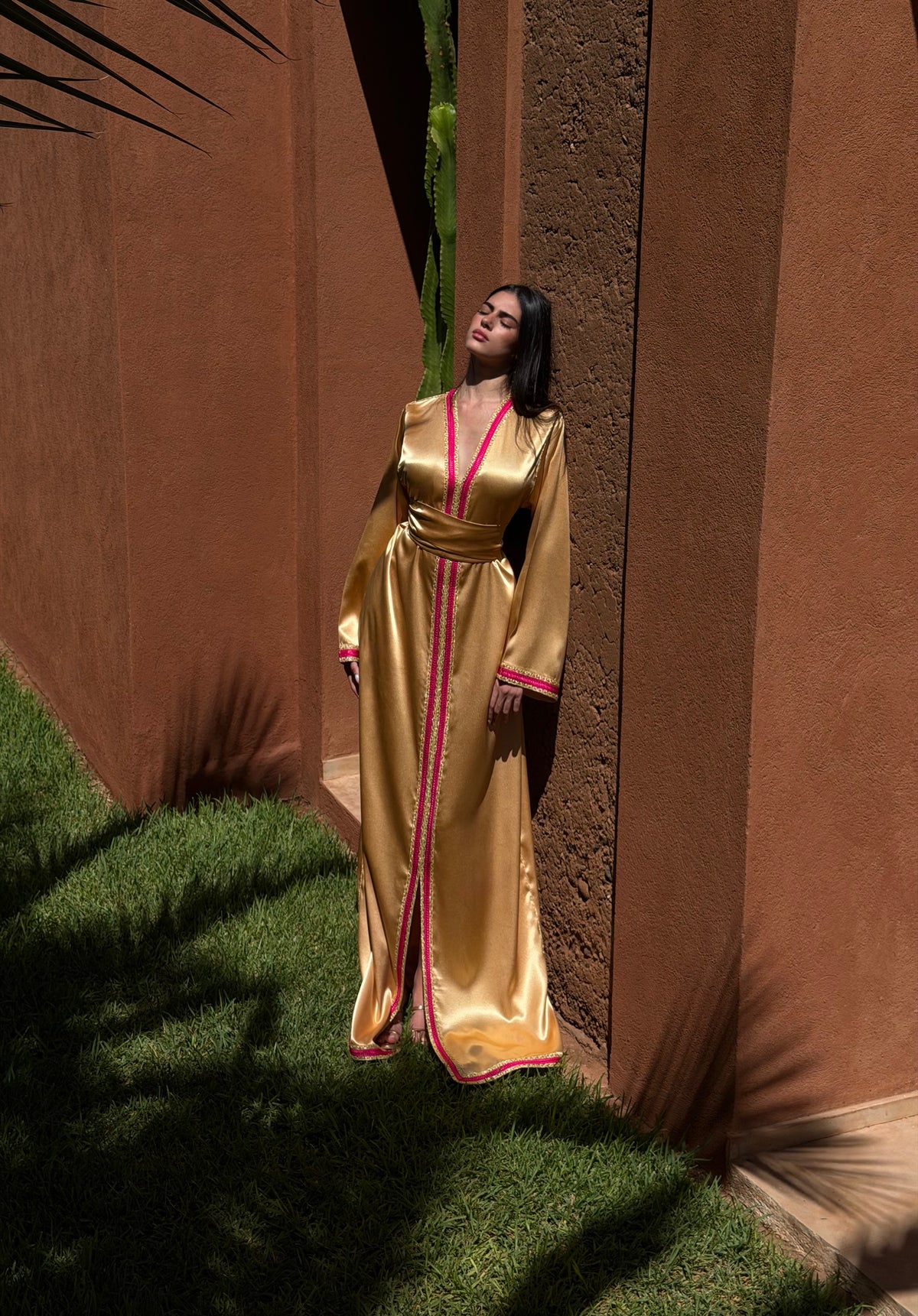Caftan Satiné Or — Silhouette en pied dans un décor extérieur.