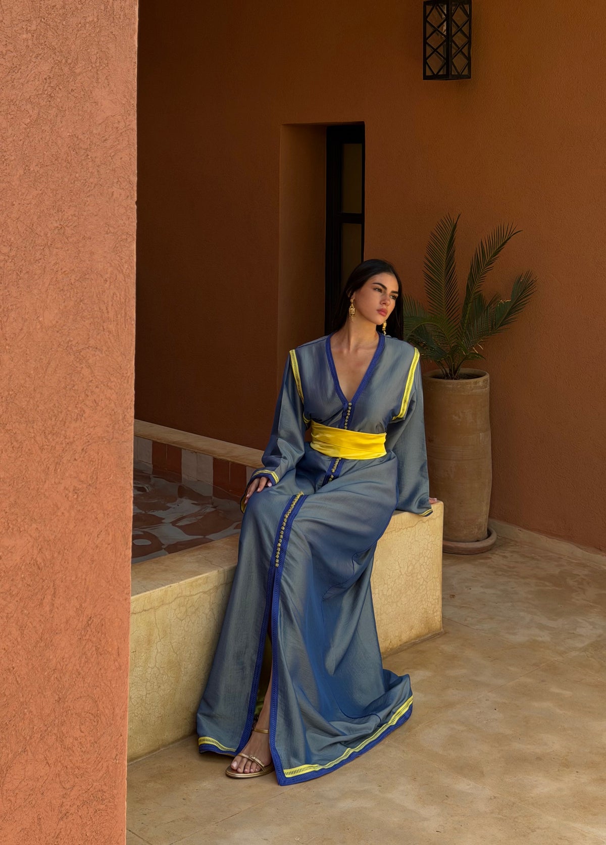 Caftan Bleu Ardoise à Ceinture Jaune — Silhouette assise dans un décor extérieur.