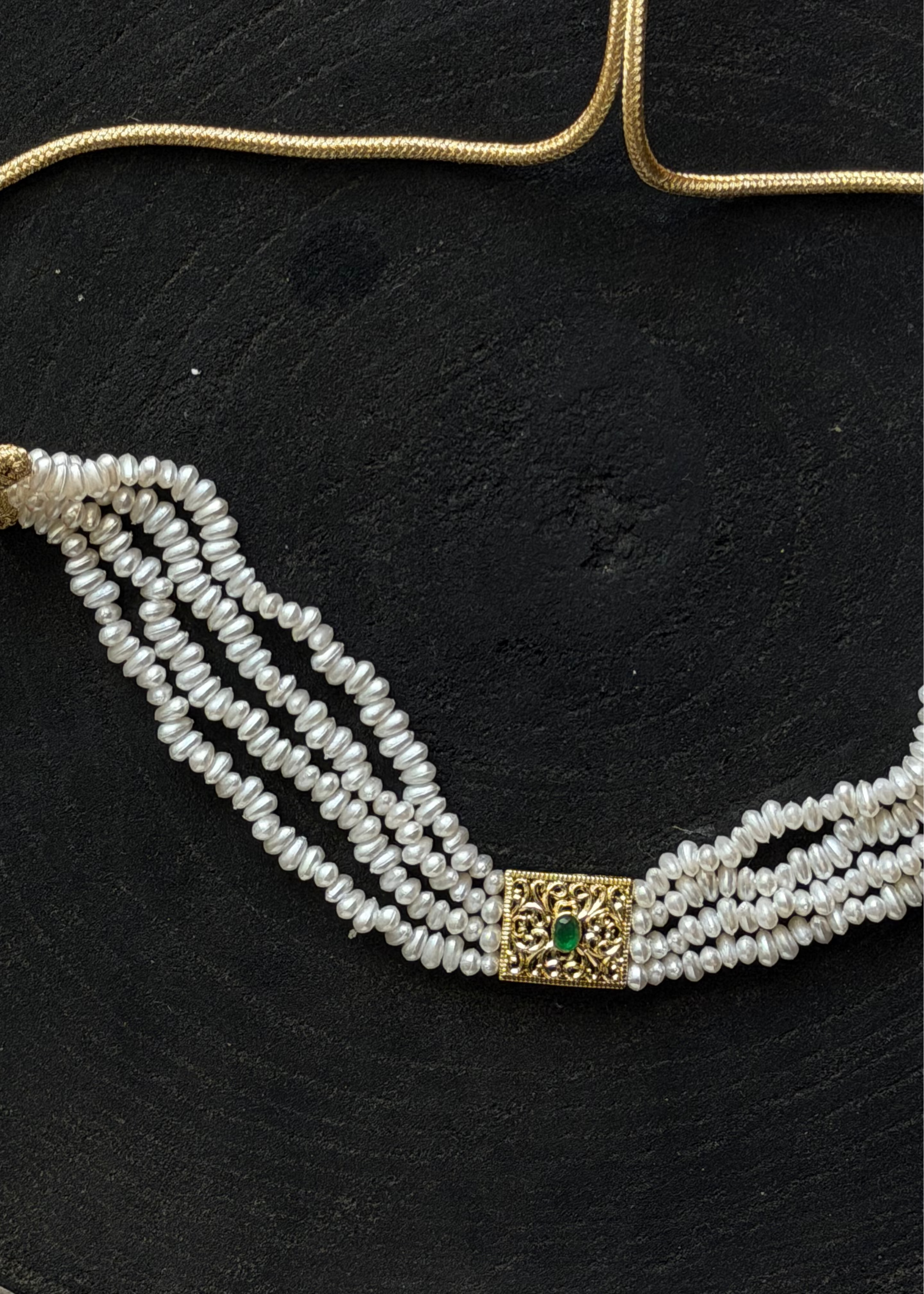 Close-up of a pearl choker featuring rows of pearlescent pearls, a gold clasp, and a central pendant adorned with a green stone