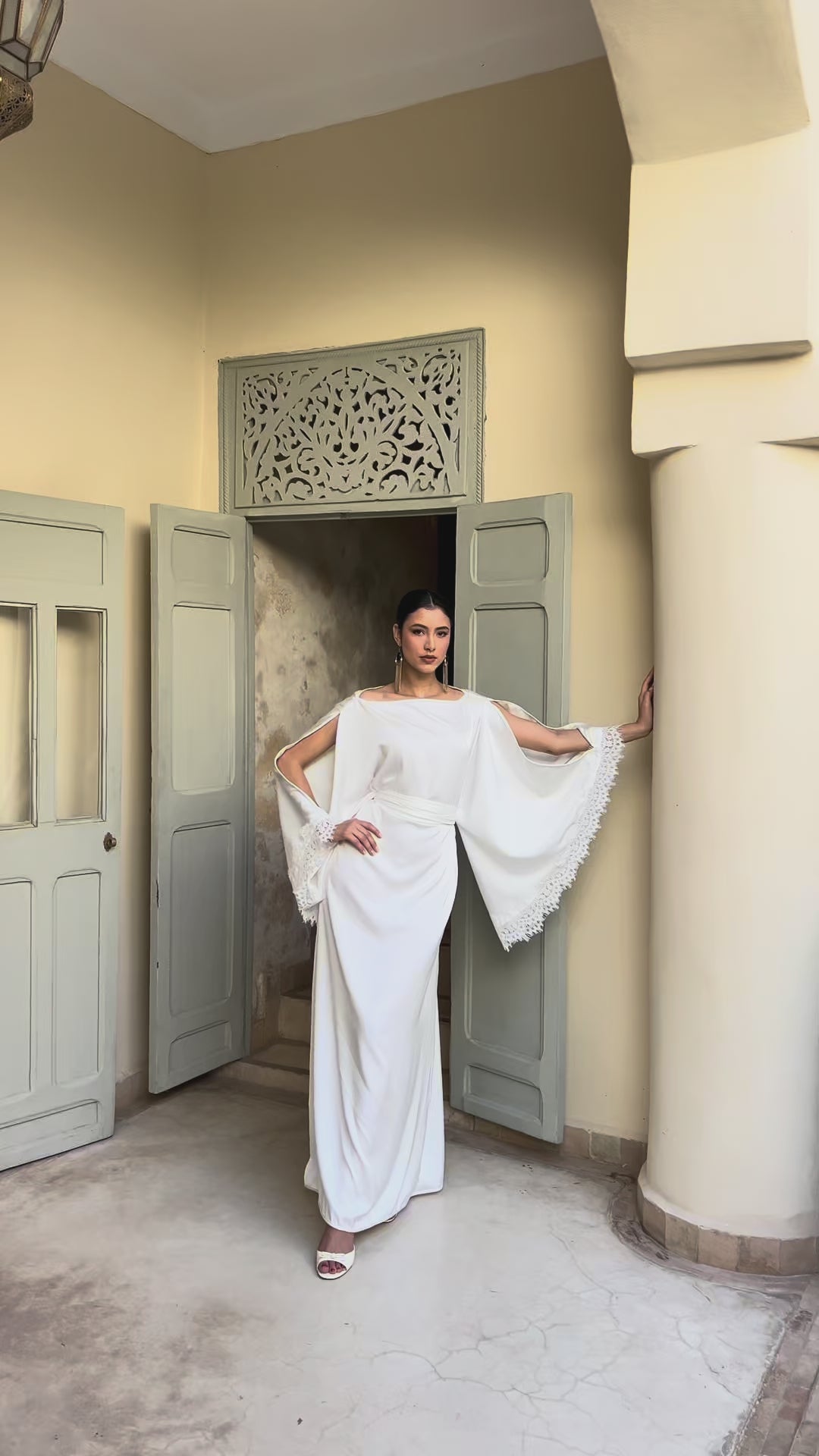 Vidéo vue de face du caftan de mariée en drap de soie blanc avec manches anges et bordures en dentelle. 