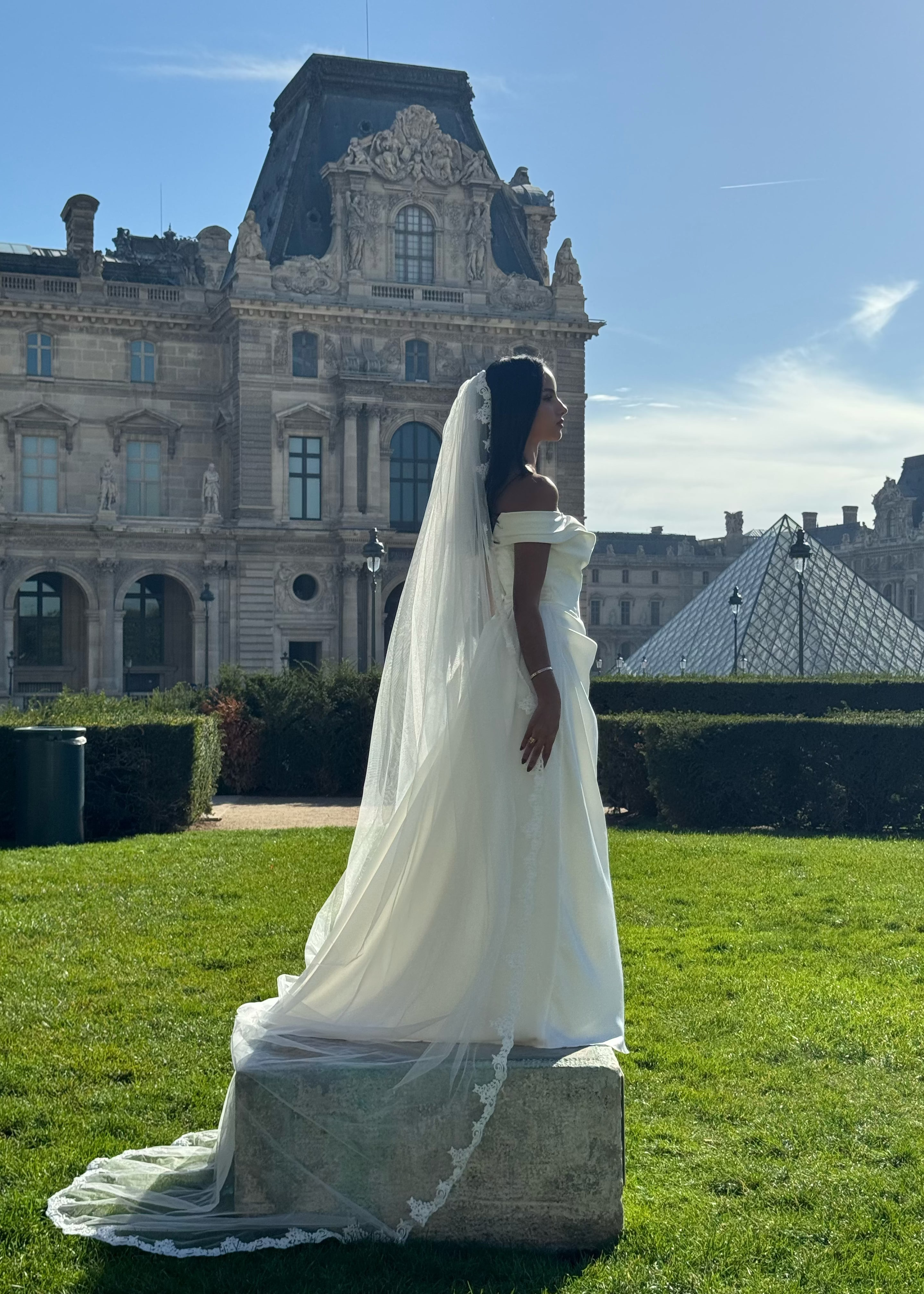 Mariée de dos avec un voile long tombant au sol, orné d'une élégante dentelle florale en bordure.