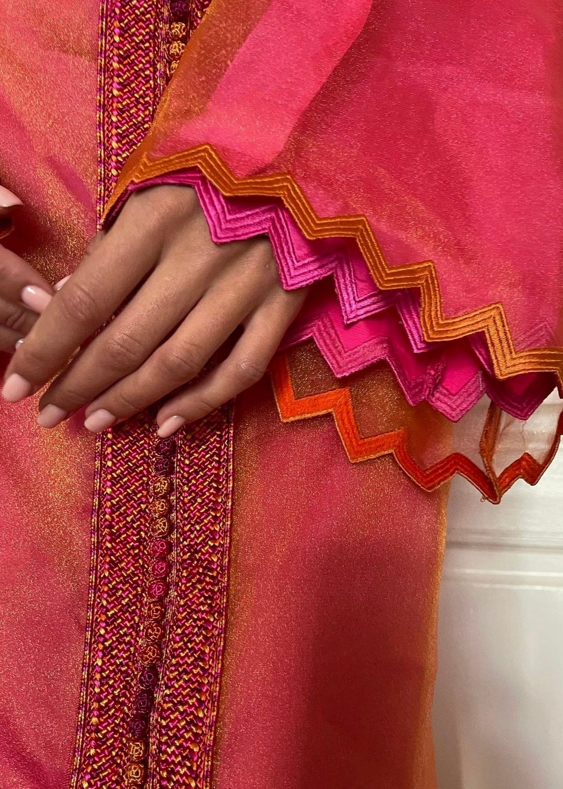 Detail of the Kaftan in orange-pink organza changeante with zigzag detailing, showing up close the iridescent texture of the fabric and the finesse of the zigzag motifs.