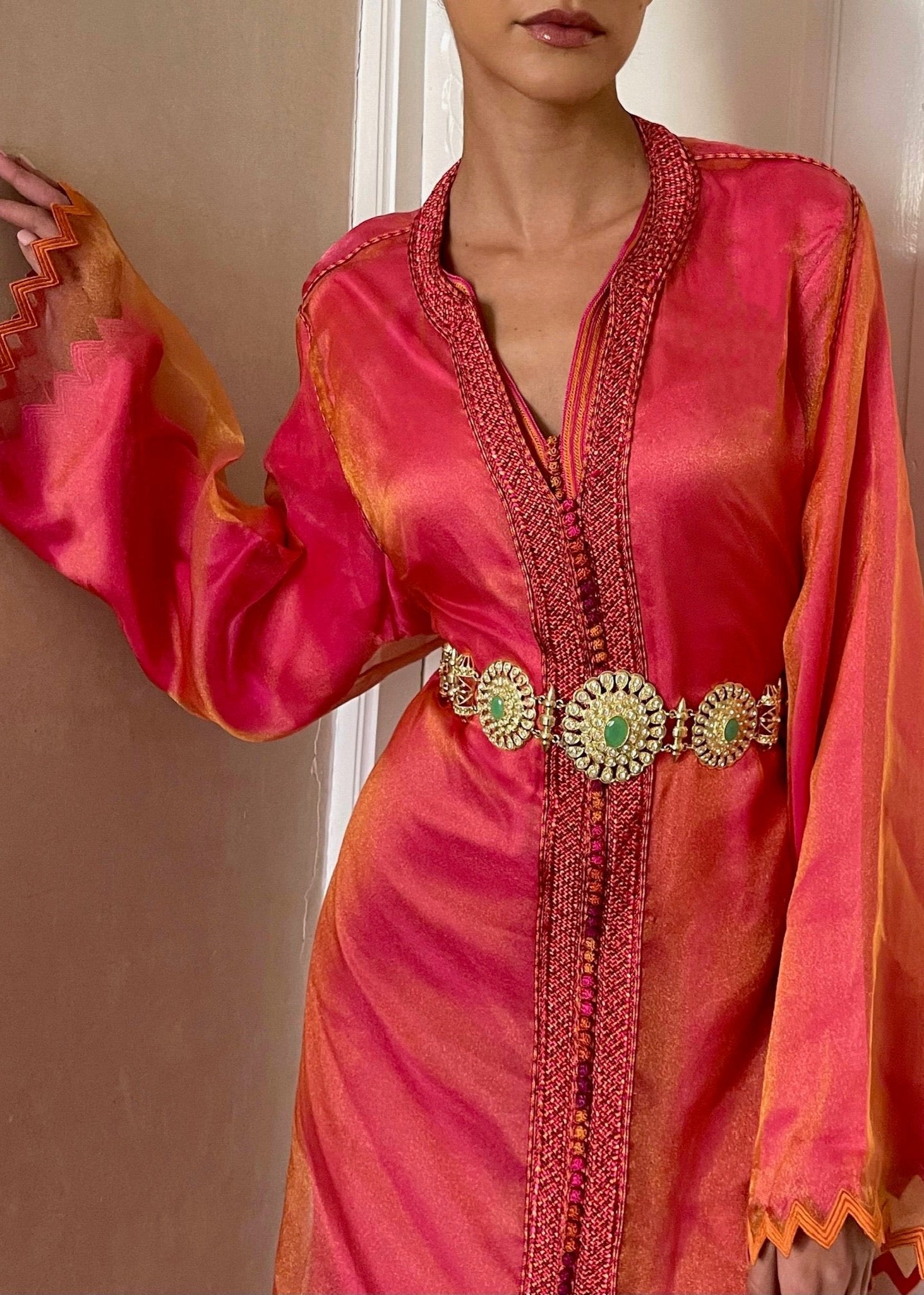 Kaftan in changeable orange-pink organza with zigzag detailing captured in motion, highlighting the fluidity of the fabric and the play of light on the patterns.