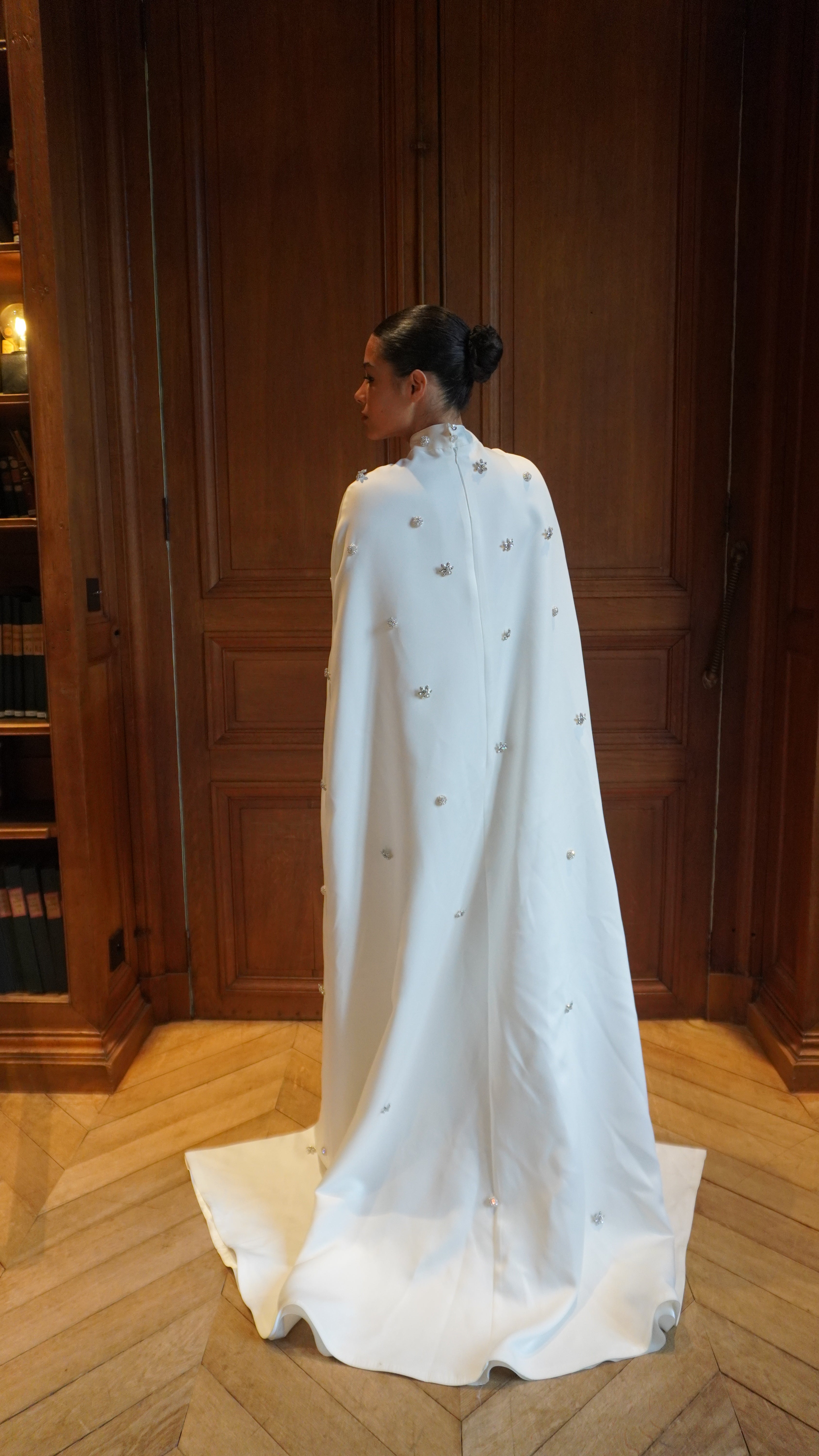 Bridal cape in palace satin with rhinestones seen from the back, highlighting the fluid fall of the fabric and the luminous reflections of the rhinestones.