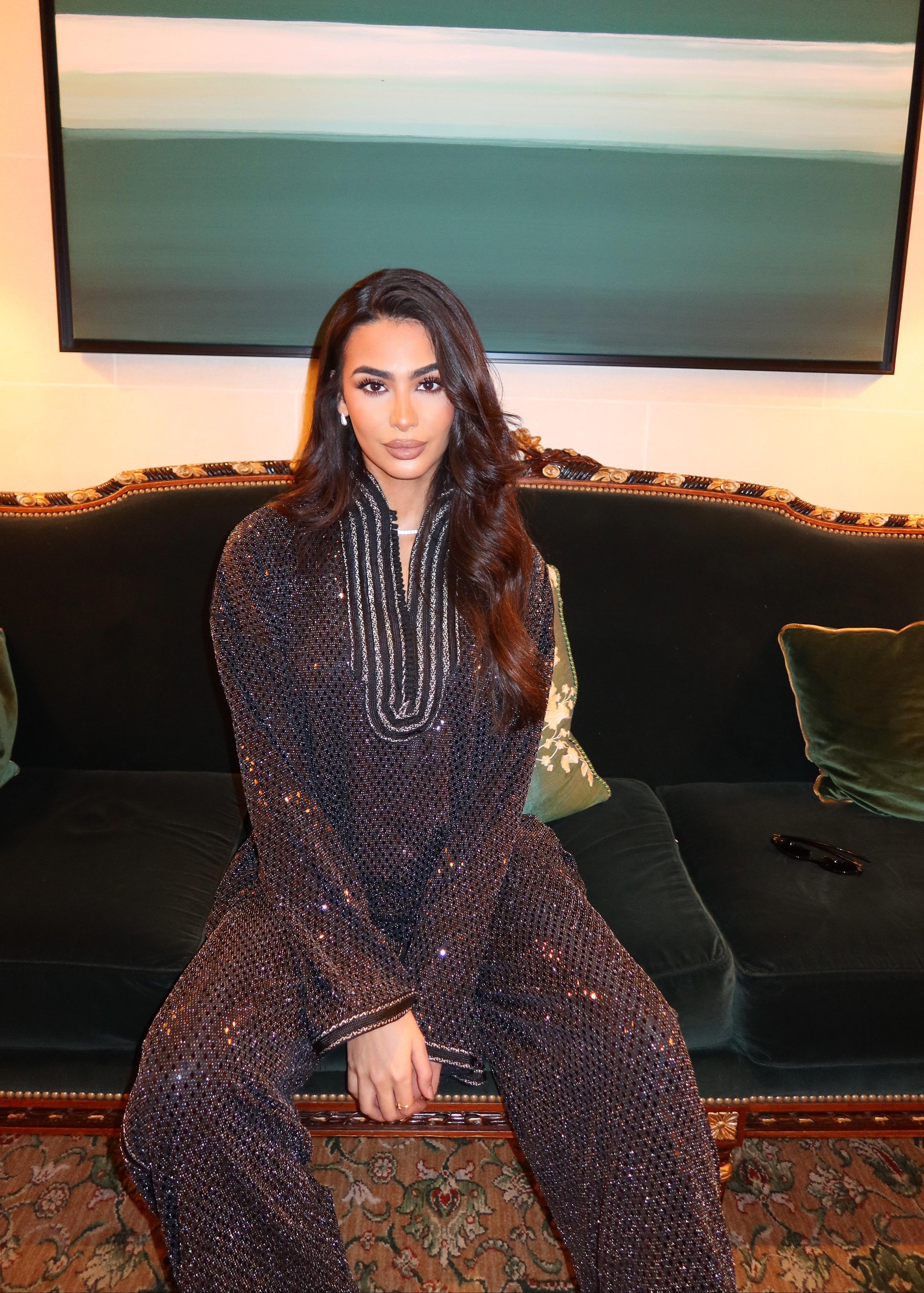 Shirt and pants ensemble in shimmering black jacquard with sfifa worn by model, elegant and contemporary style inspired by Moroccan craftsmanship. Seated photo.