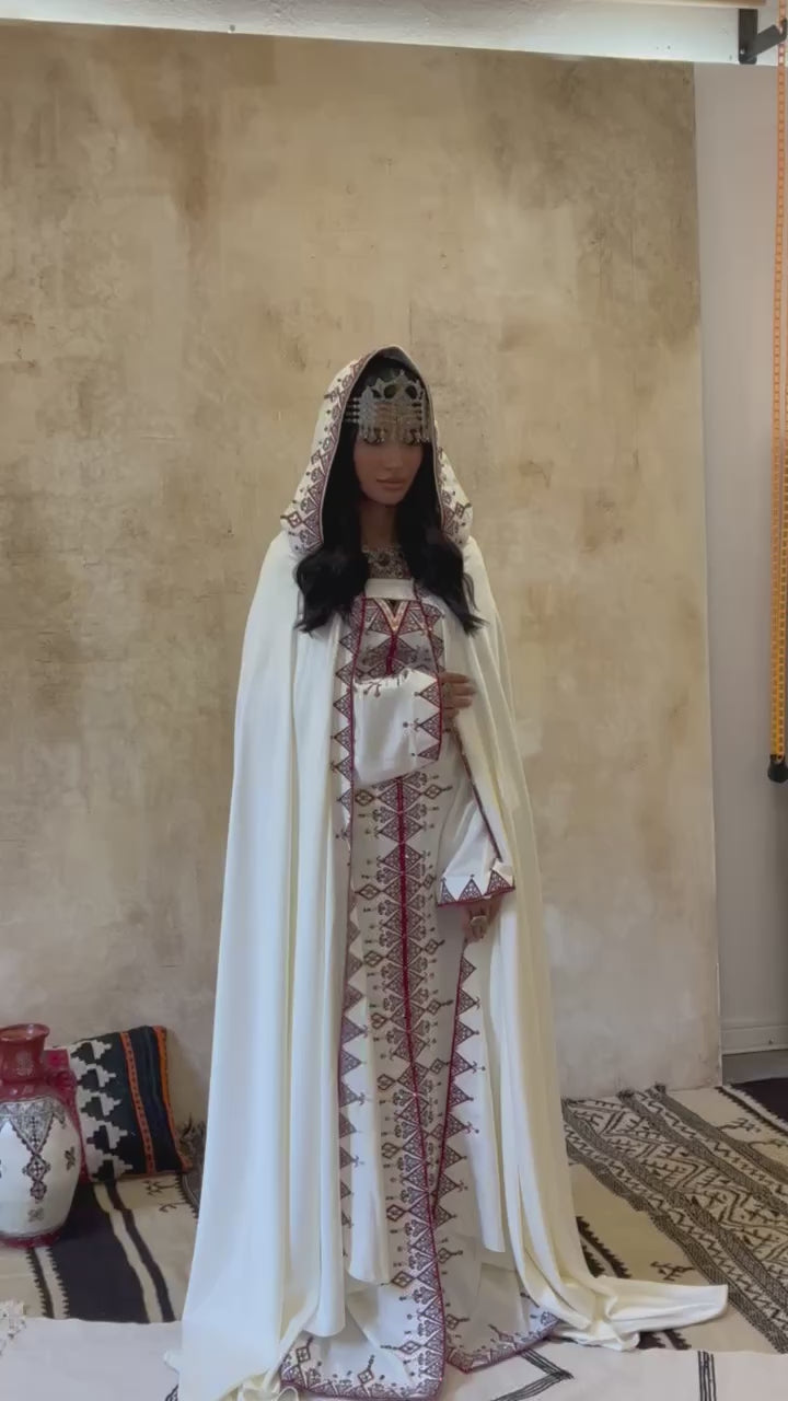 Video of a traditional Kabyle embroidered wedding dress, accompanied by a matching burnous, worn by a bride, showcasing Berber patterns, colorful embroidery, and the ceremonial wearing of the ensemble.