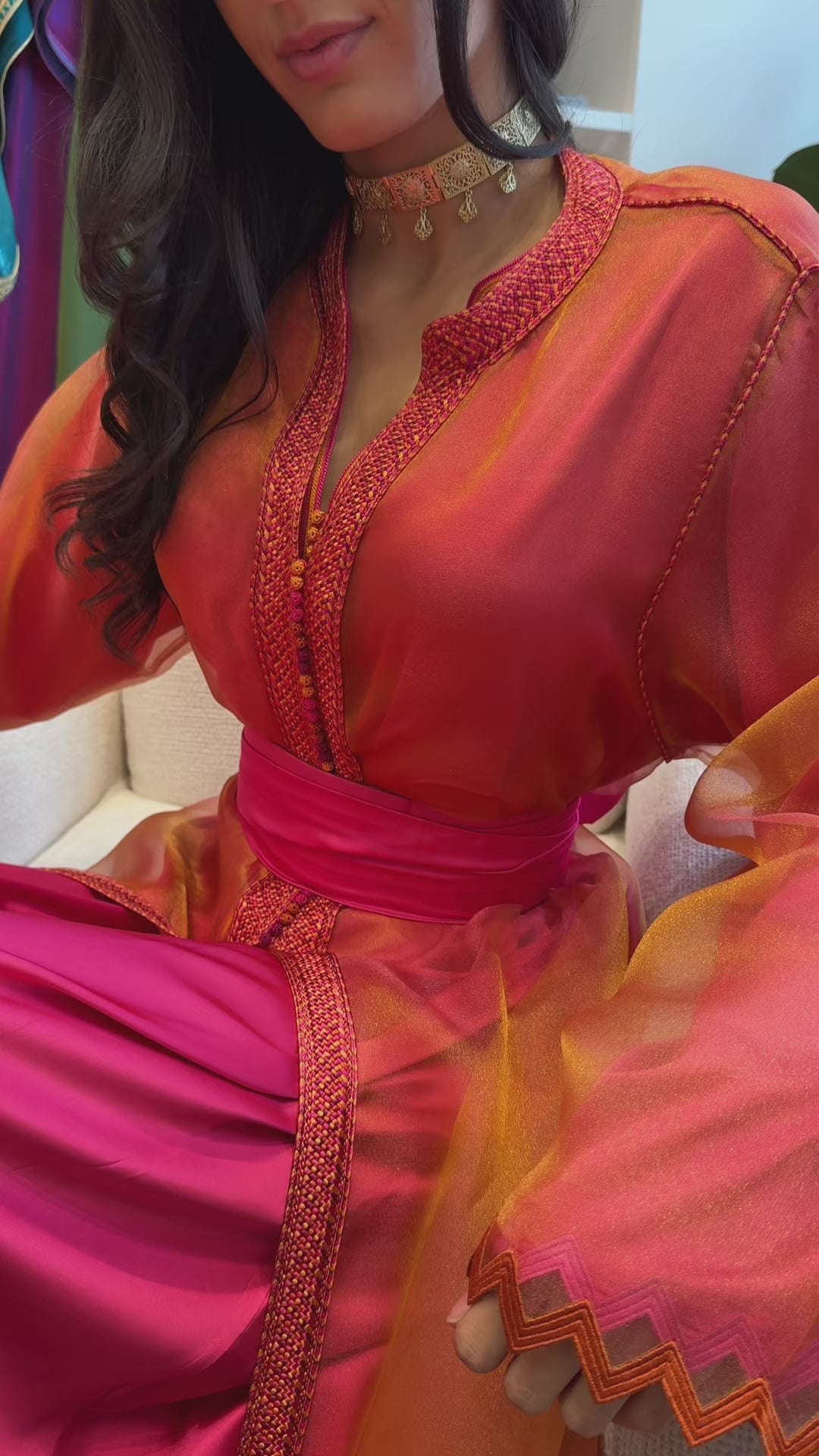 Video of a changing organza Kaftan in shades of orange and pink, with distinctive zigzag details, worn by a moving model to reveal the reflections and fluidity of the fabric.
