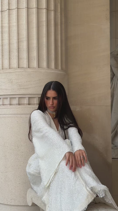 Video of a beaded bridal Kaftan with flared sleeves, revealing embroidered and glittering details. The model scrolls slowly, highlighting the fluidity of the sleeves and the sparkle of the fabric under the light.