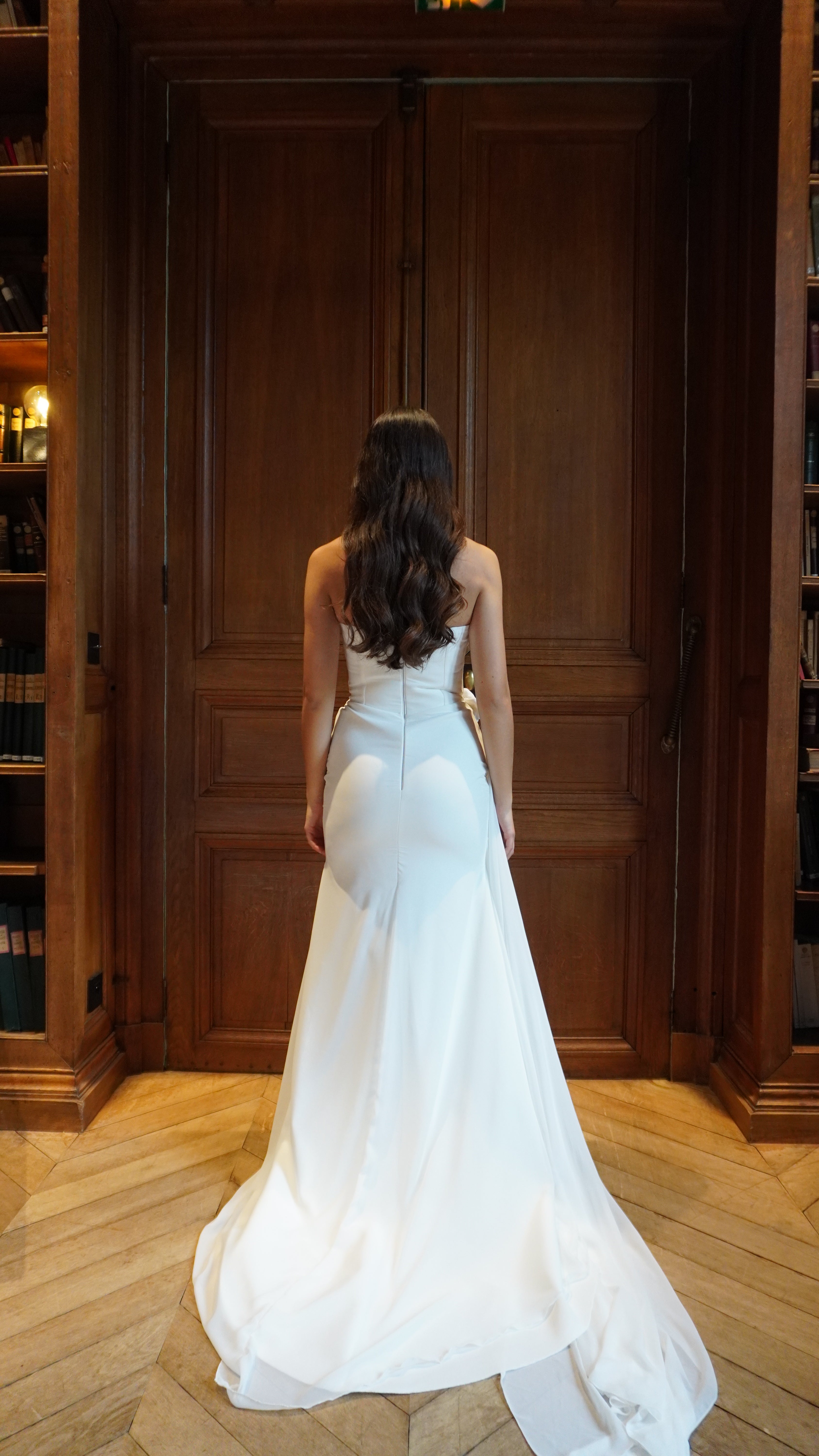 Draped mermaid wedding gown with removable flower seen from the back, revealing sophisticated lines and a flattering cut.